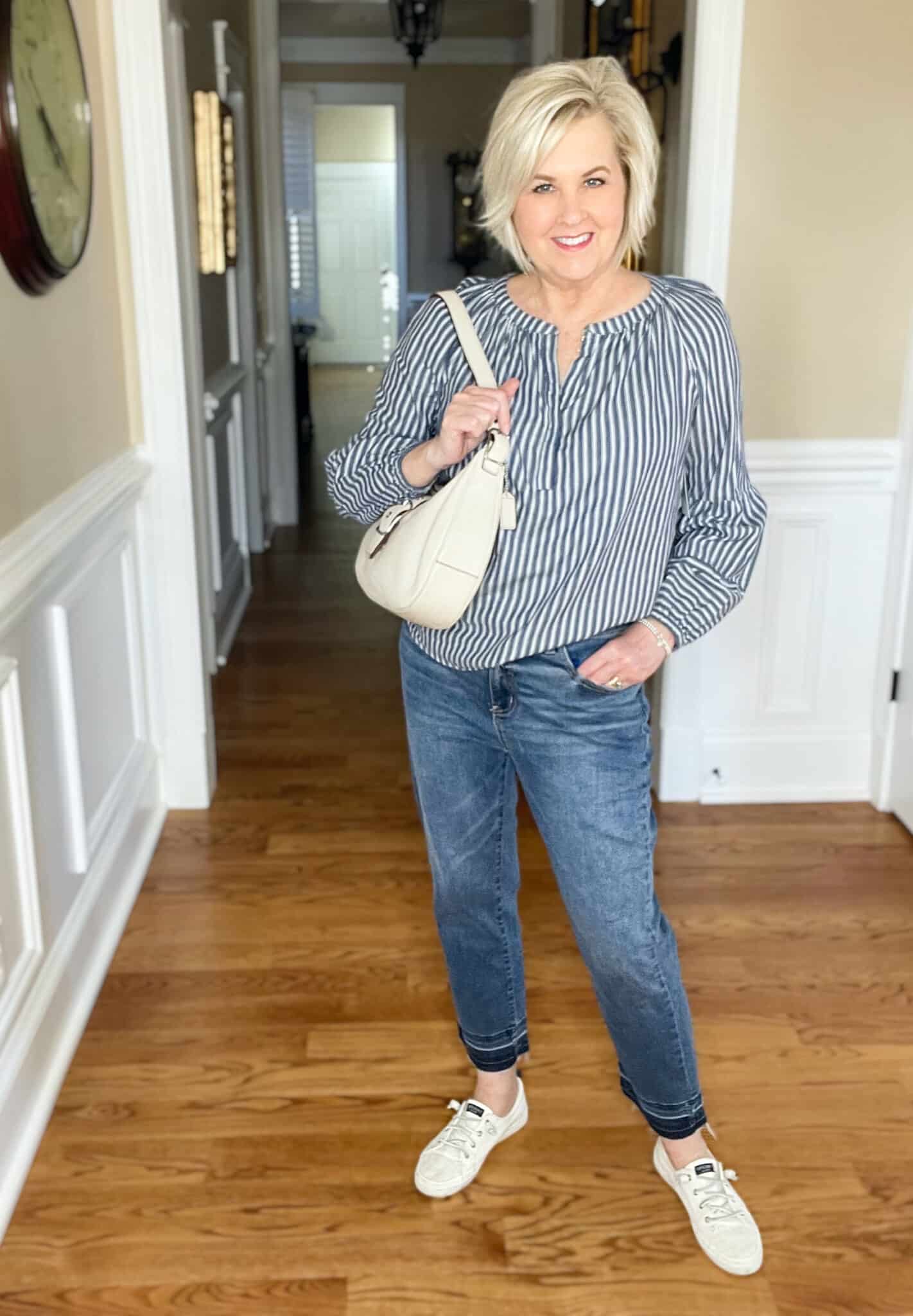 Over 40 Fashion Blogger, Tania Stephens is styling a pair of released hem jeans with sneakers, an ivory shoulder bag, and a striped shirt