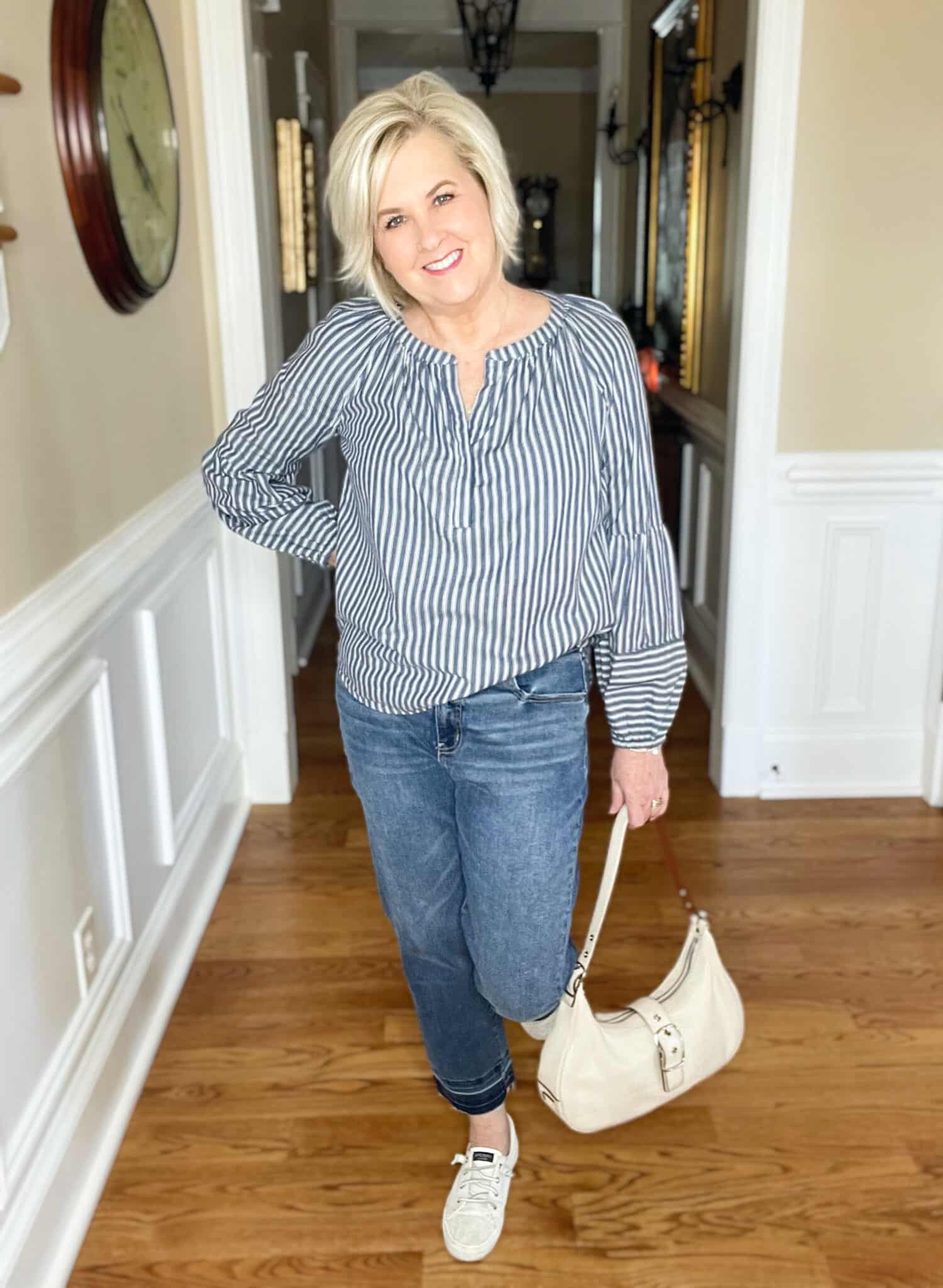 Over 40 Fashion Blogger, Tania Stephens is styling a pair of released hem jeans with sneakers, a striped shirt, and a coach handbag