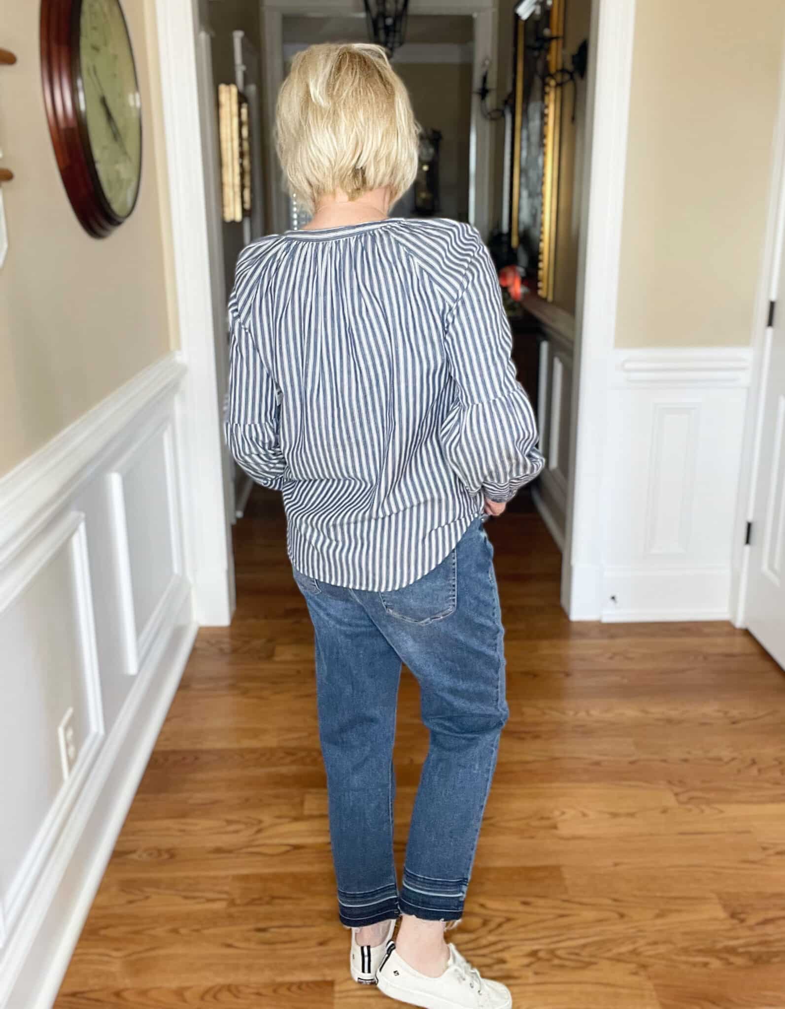 Over 40 Fashion Blogger, Tania Stephens is showing the back of a pair of released hem jeans with sneakers and a striped shirt