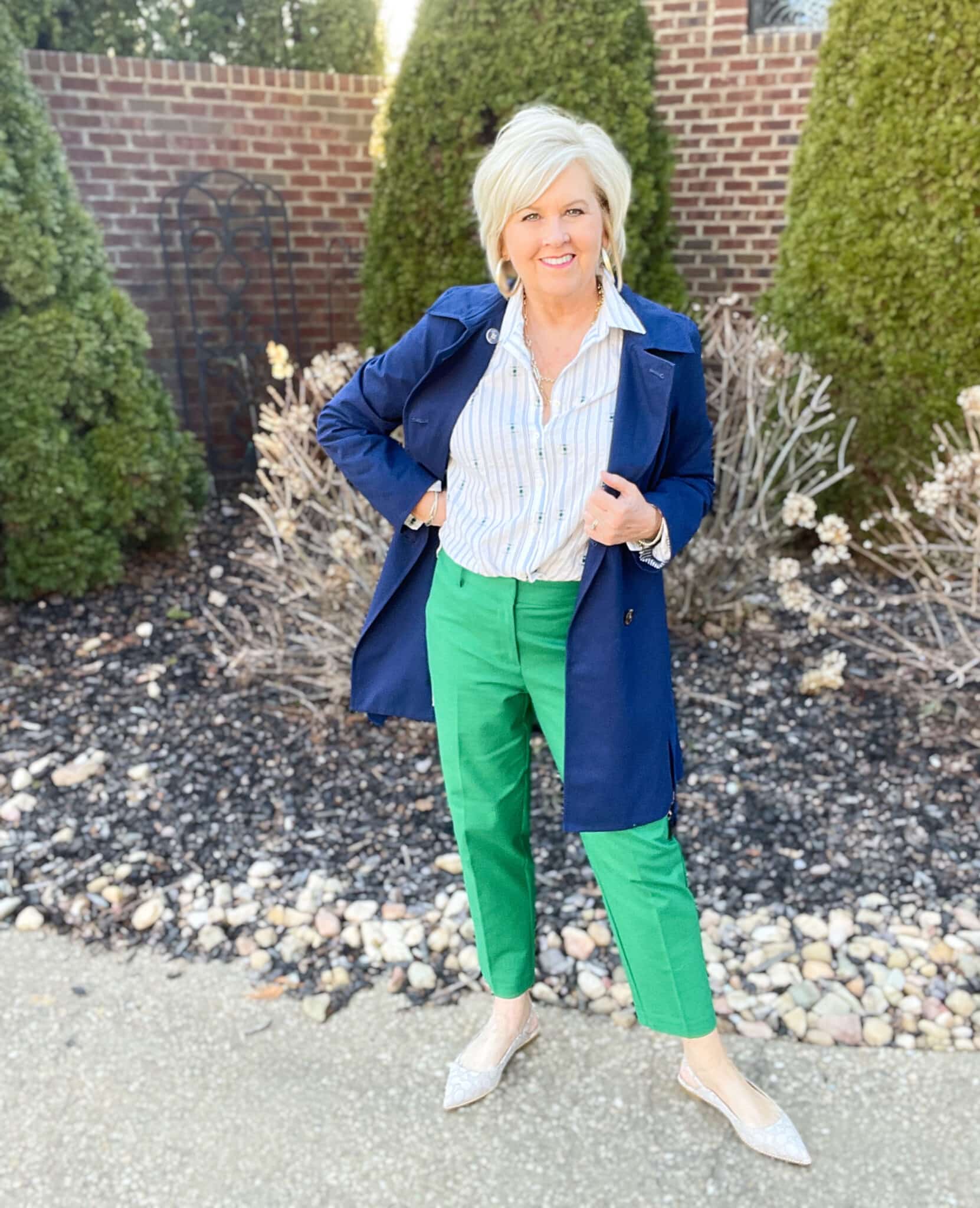 Over 40 Fashion Blogger, Tania Stephens is wearing green pants, a white printed button up shirt, and a navy trench coat