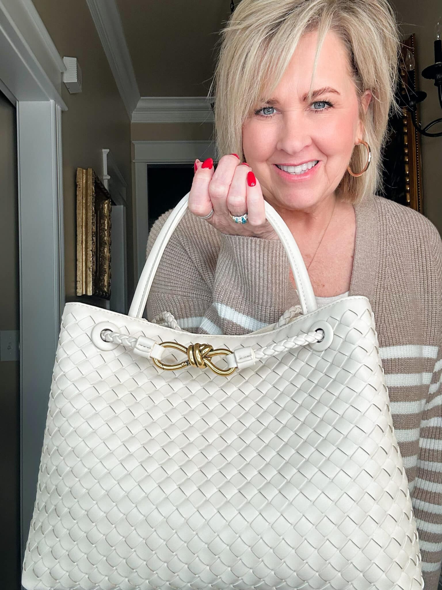 Over 50 Fashion Blogger, Tania Stephens is holding a woven handbag with a bow detail 1