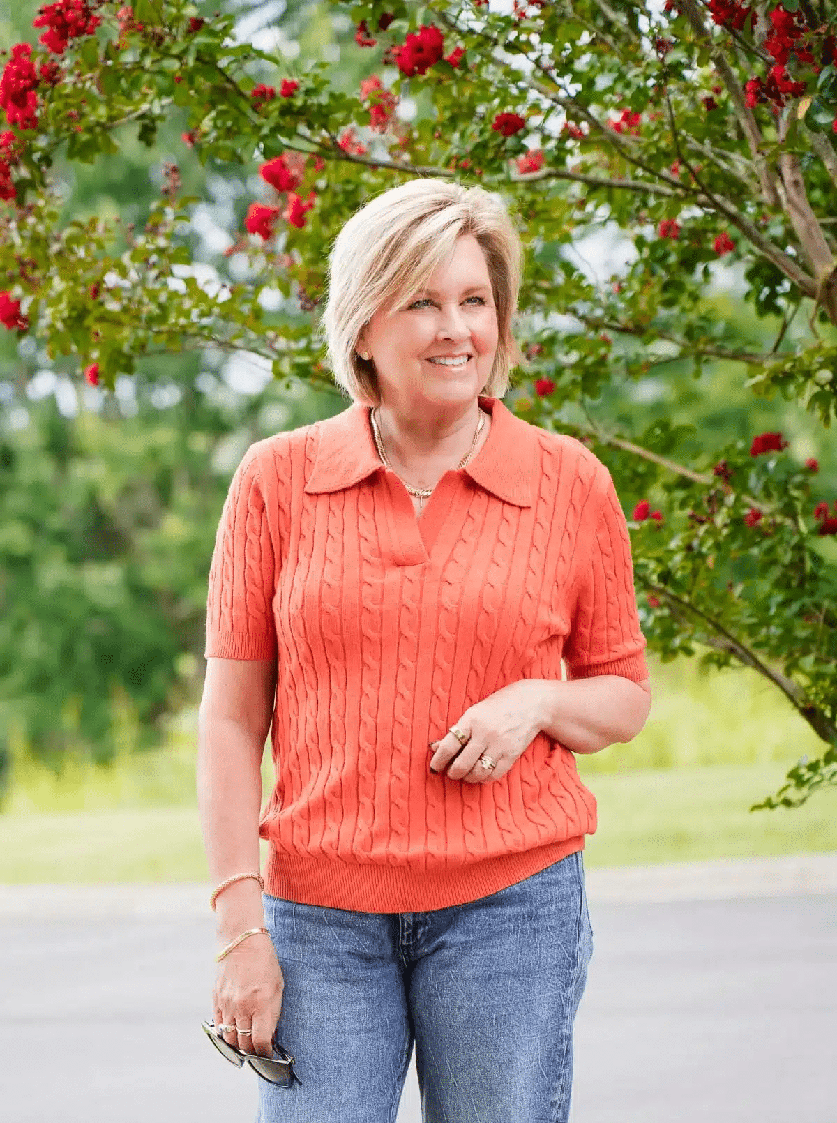 Tania Stephens wearing a rust red short sleeve cable knit sweater styled with white jeans, an example of how to wear earth tones in summer with warmth and texture.