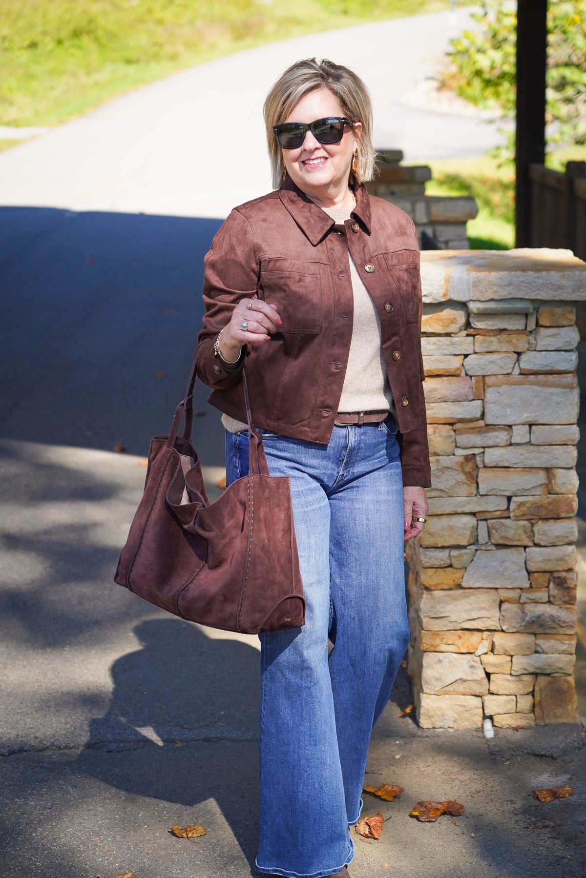 Tania Stephens is styling Trending Chocolate Brown This Fall with a brown faux suede jacket, a tan camel cashmere sweater, wide leg Mother jeans, and a dark brown suede tote
