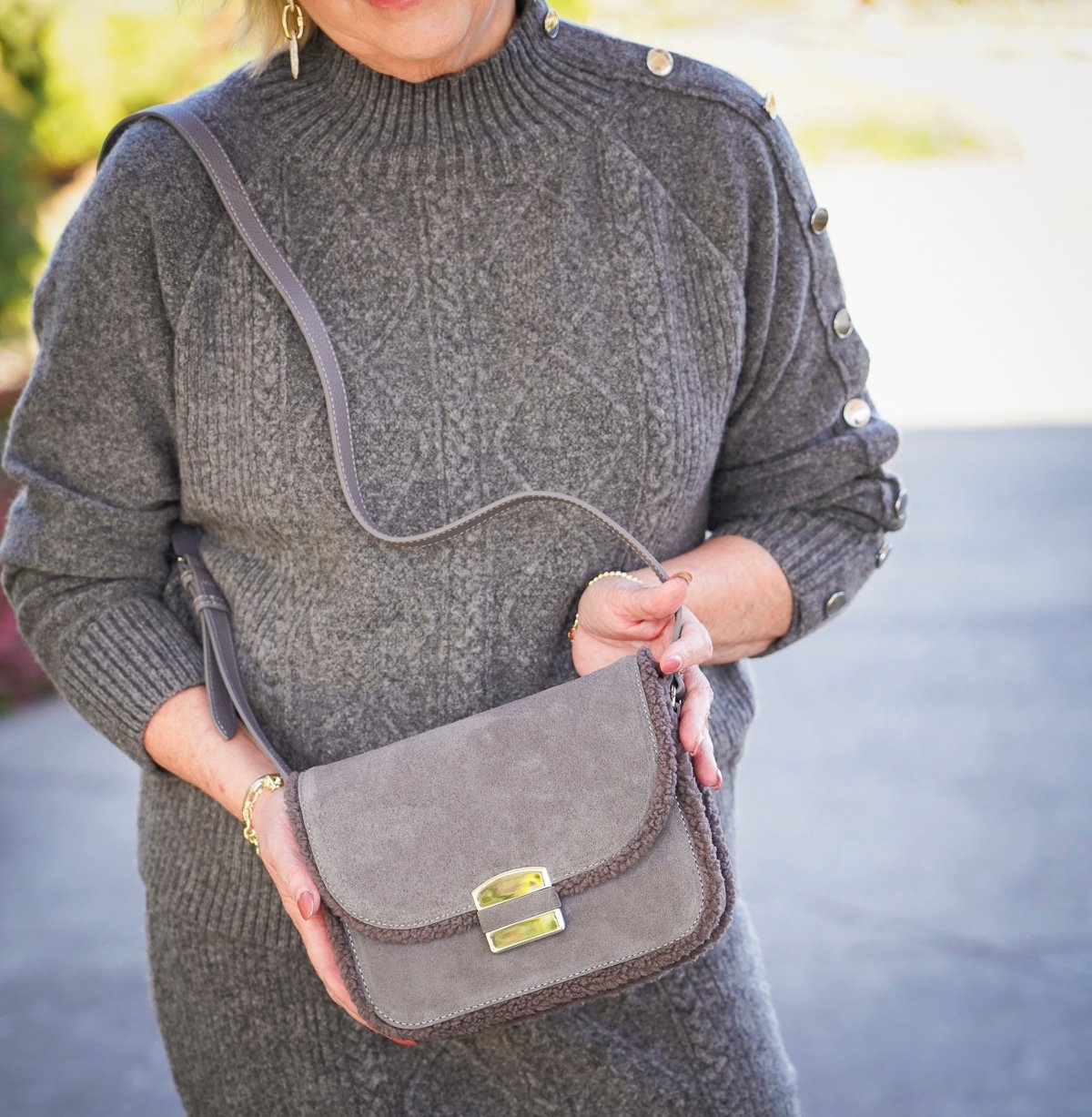 Tania Stephens is wearing a gray cable knit sweater and gray crossbody