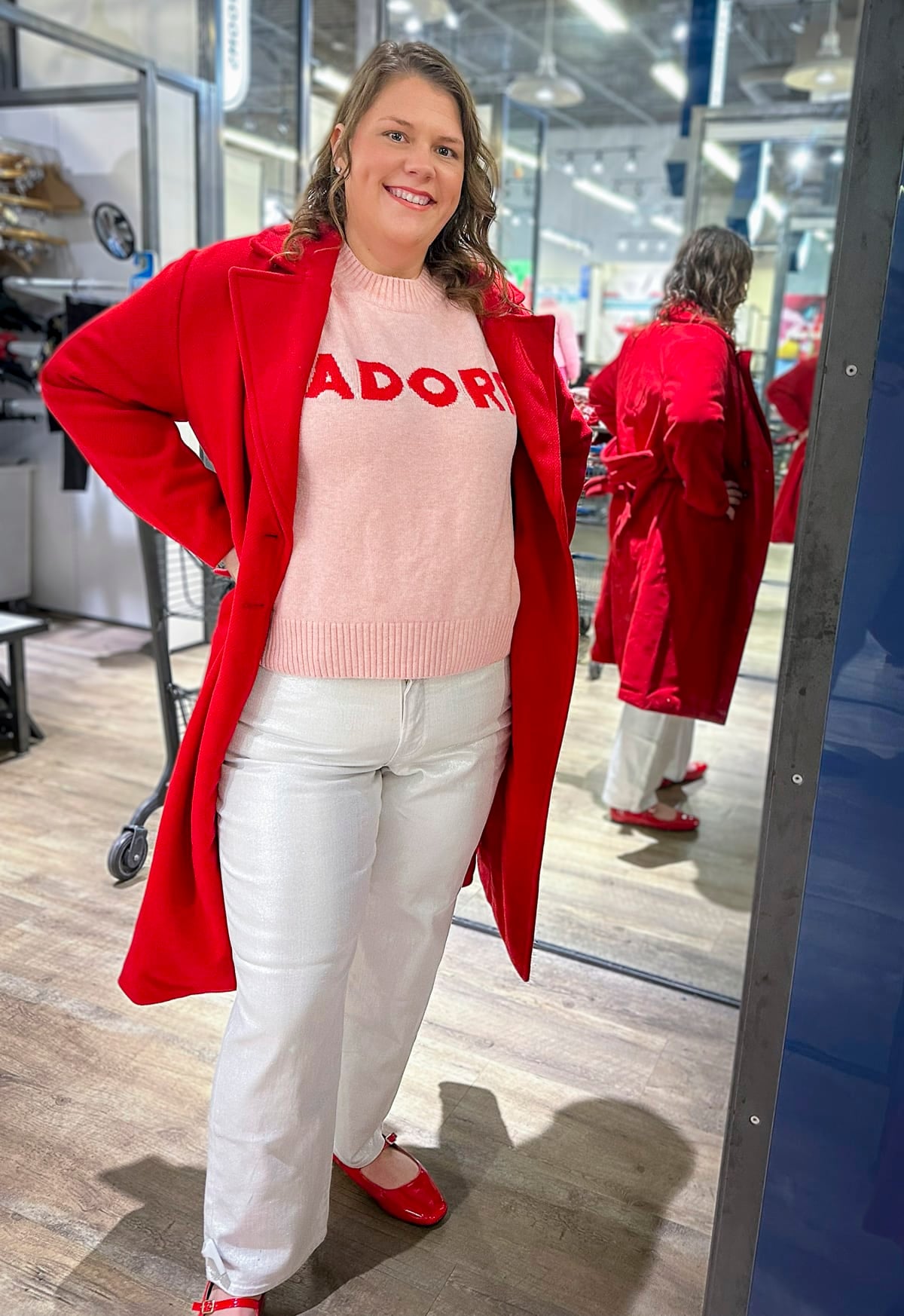 Megan is wearing a pink sweater, white jeans, and a red coat