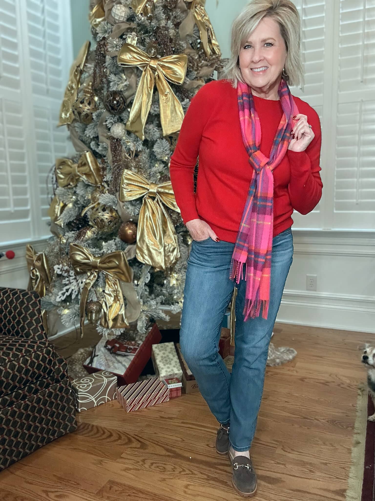 Tania Stephens is wearing a soft, red sweater, a pink plaid scarf, and straight-leg jeans