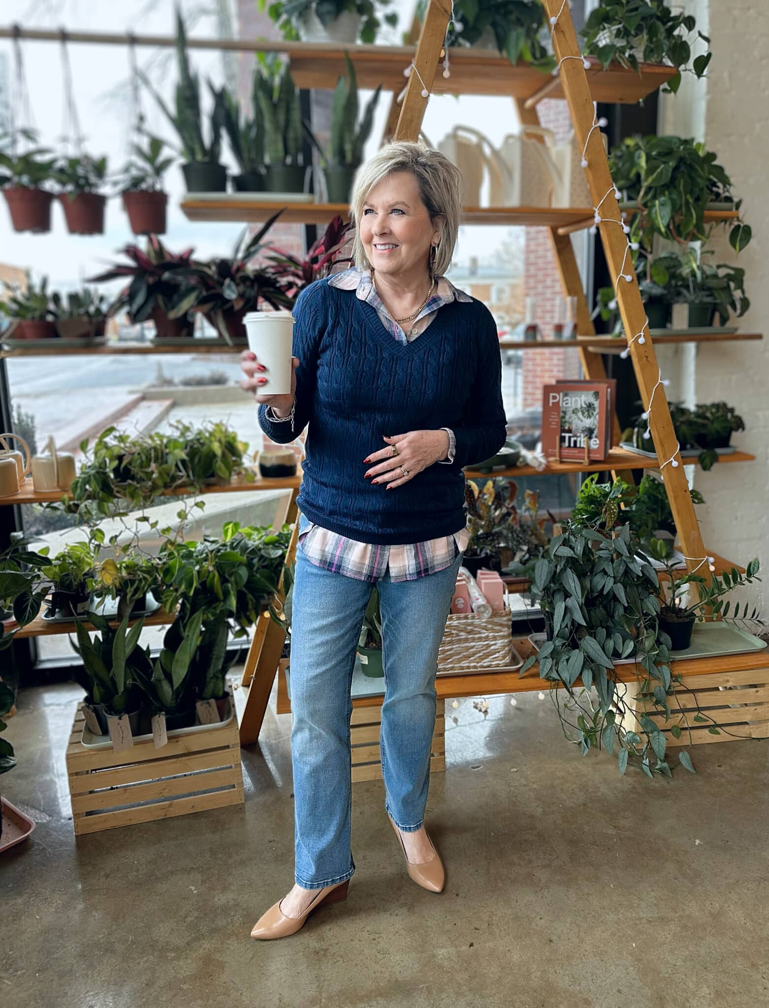 Tania Stephens is holding a cup of coffee while wearing a plaid shirt under a navy sweater and straight leg jeans from Kohl's
