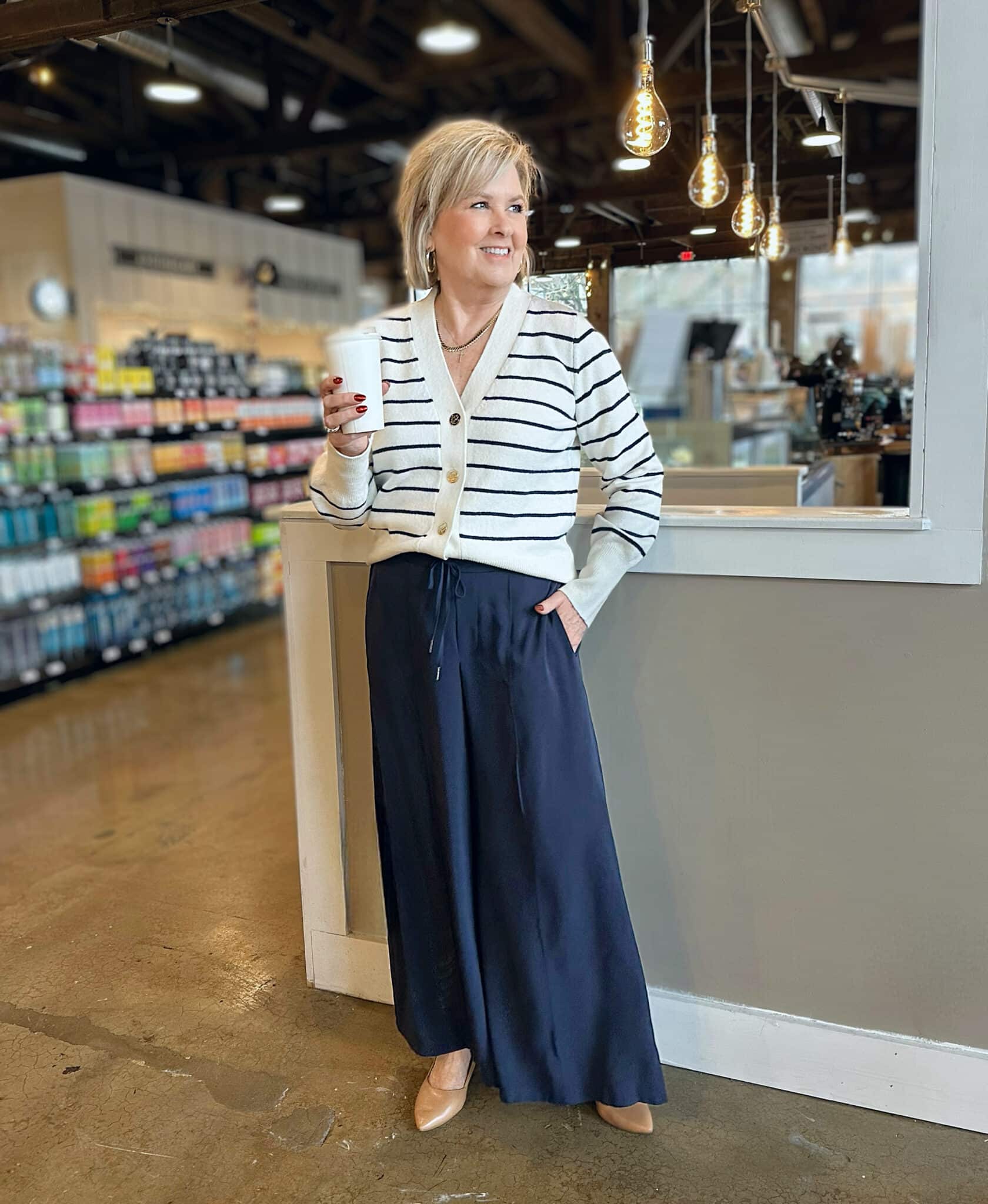 Tania Stephens is holding a cup of coffee while wearing a striped sweater and navy palazzo pants from Kohl's