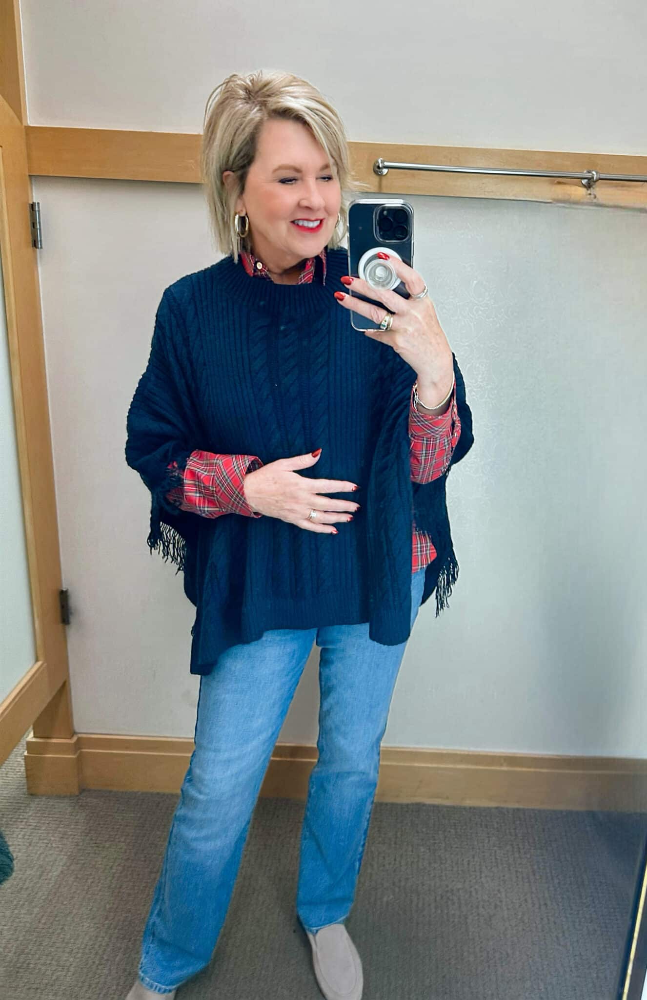 Tania Stephens is wearing a plaid button up shirt, a navy poncho, and barely boot cut jeans