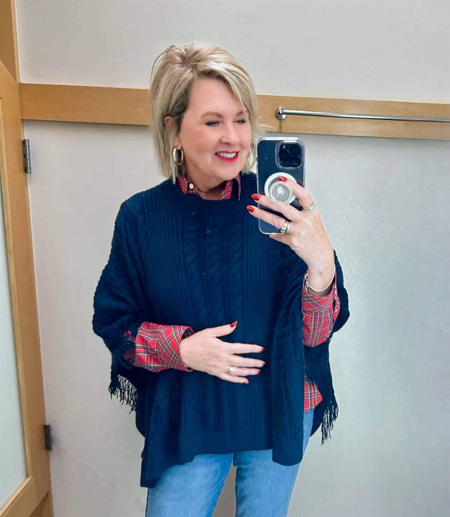 Tania Stephens is wearing a plaid button up shirt, a navy poncho, and barely boot cut jeans