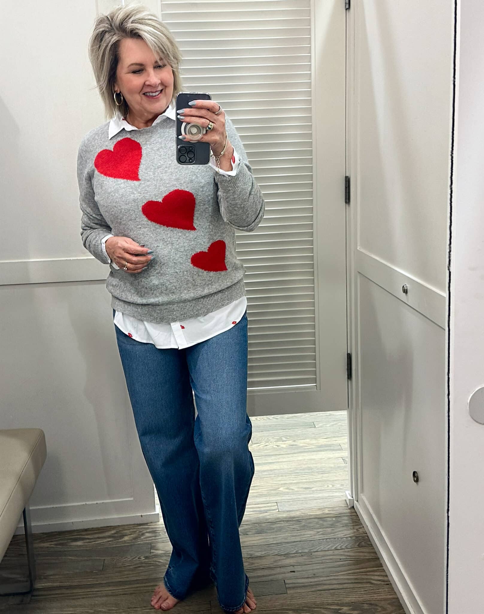 Tania Stephens is wearing a heart sweater, a button up shirt, and wide leg jeans