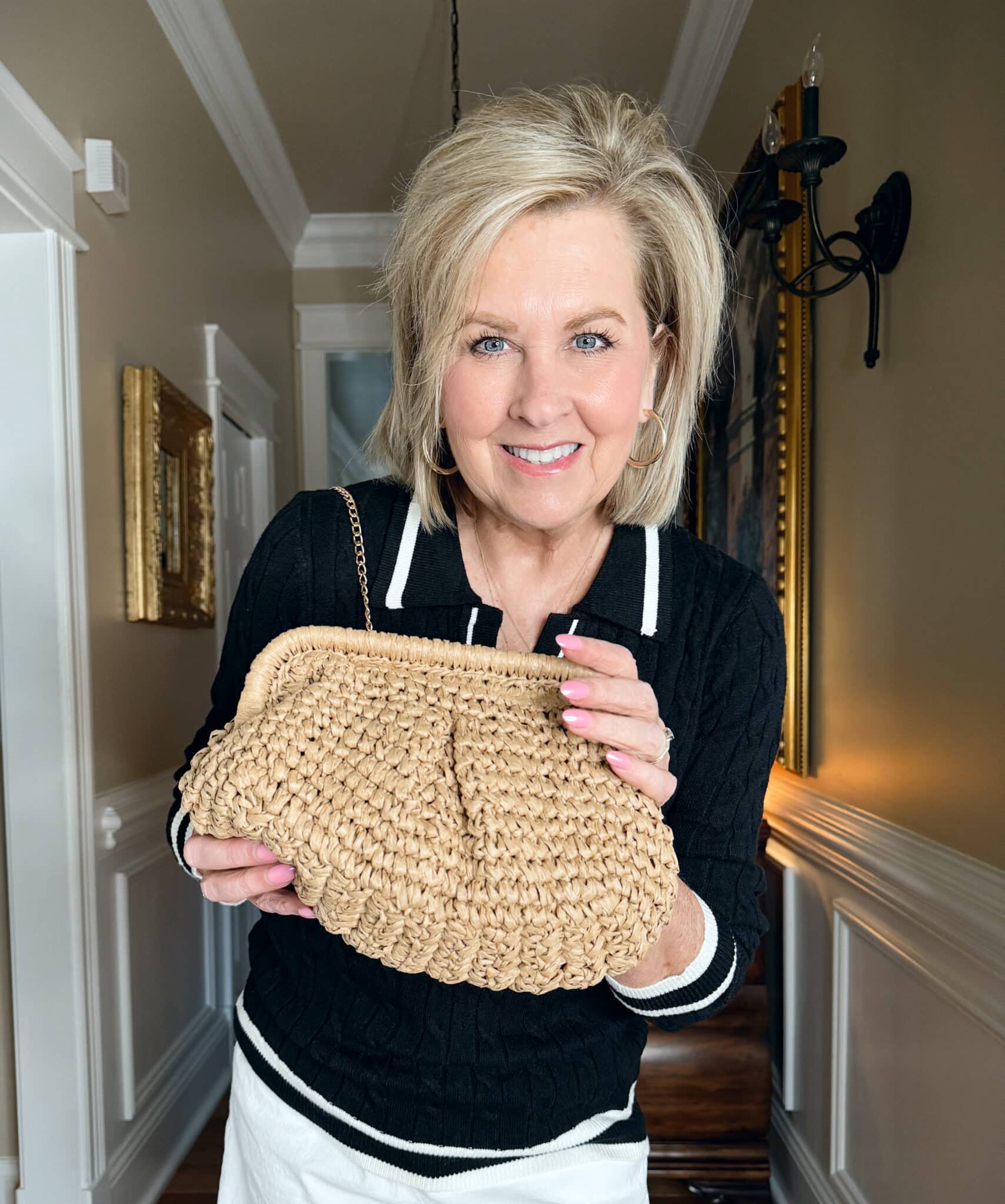 Tania Stephens is wearing a black cable knit sweater and holding a raffia crossbody handbag