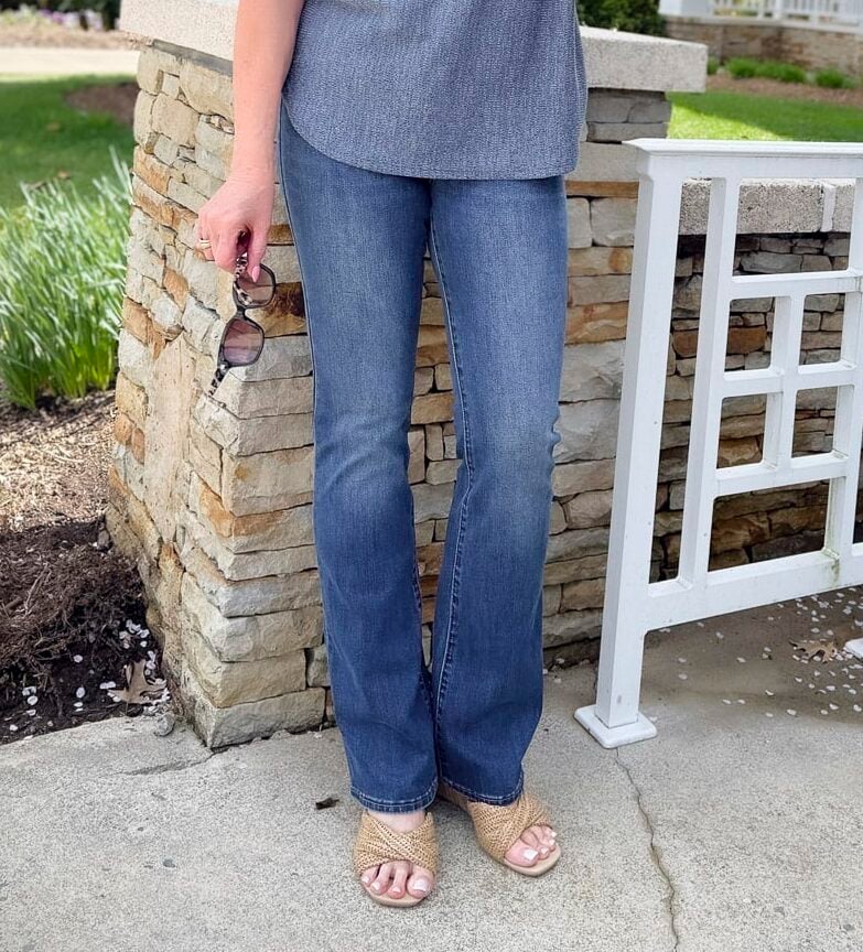 a woman wearing jeans and holding a pair of sunglasses