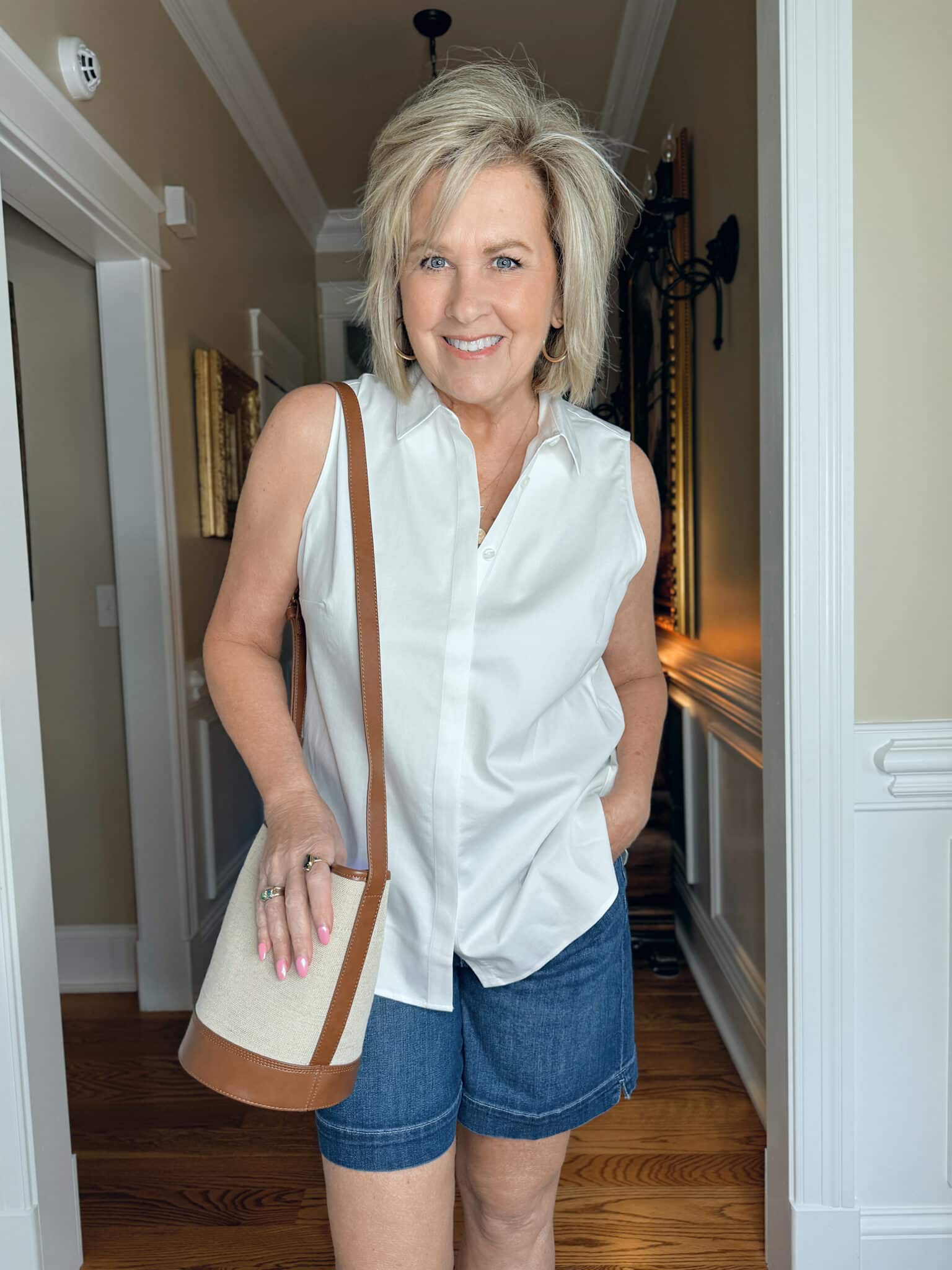 Woman over 50 wearing a sleeveless white button-up shirt with dark denim shorts