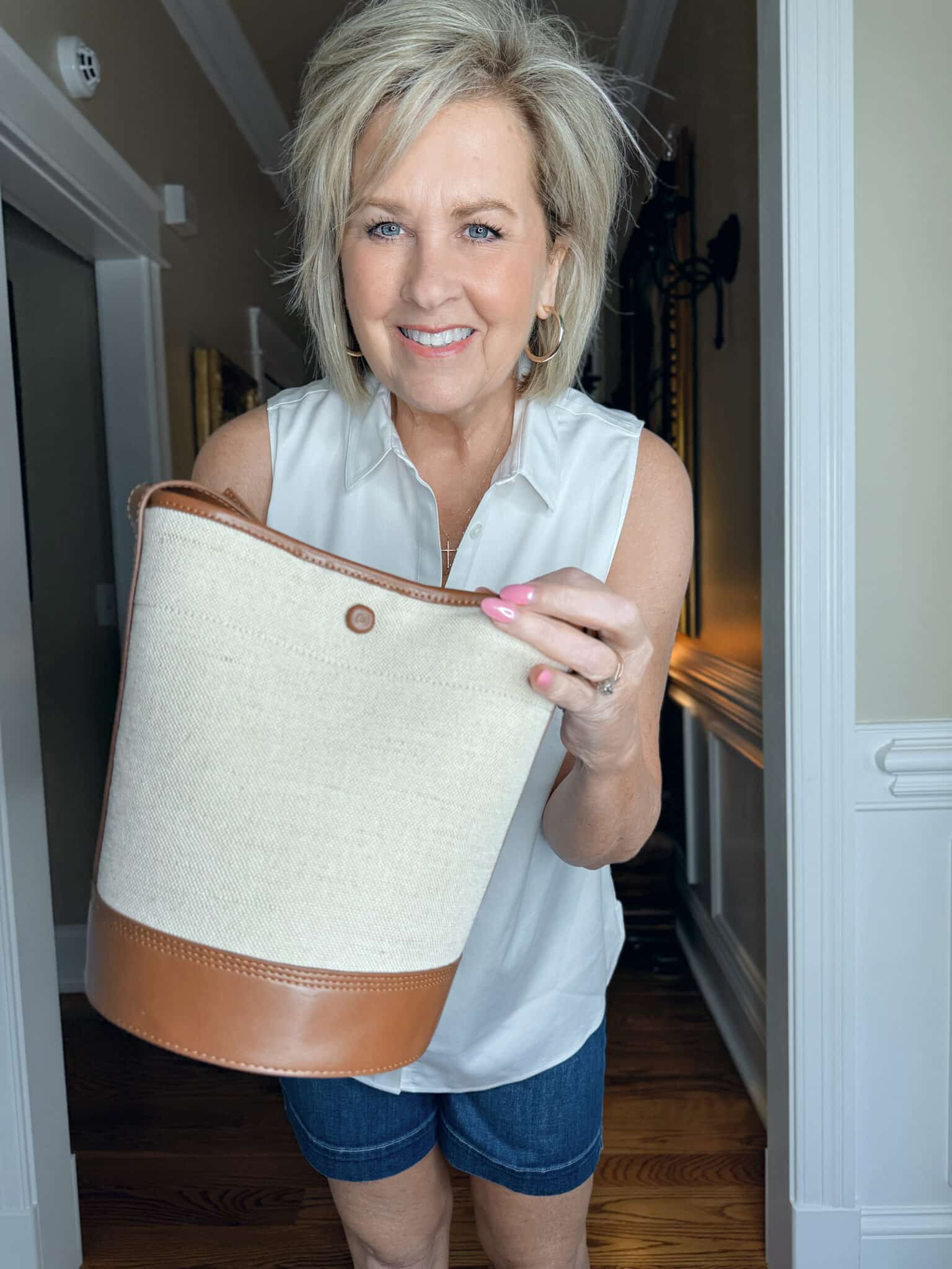 Woman over 50 wearing a sleeveless white button-up shirt with a canvas bucket bag