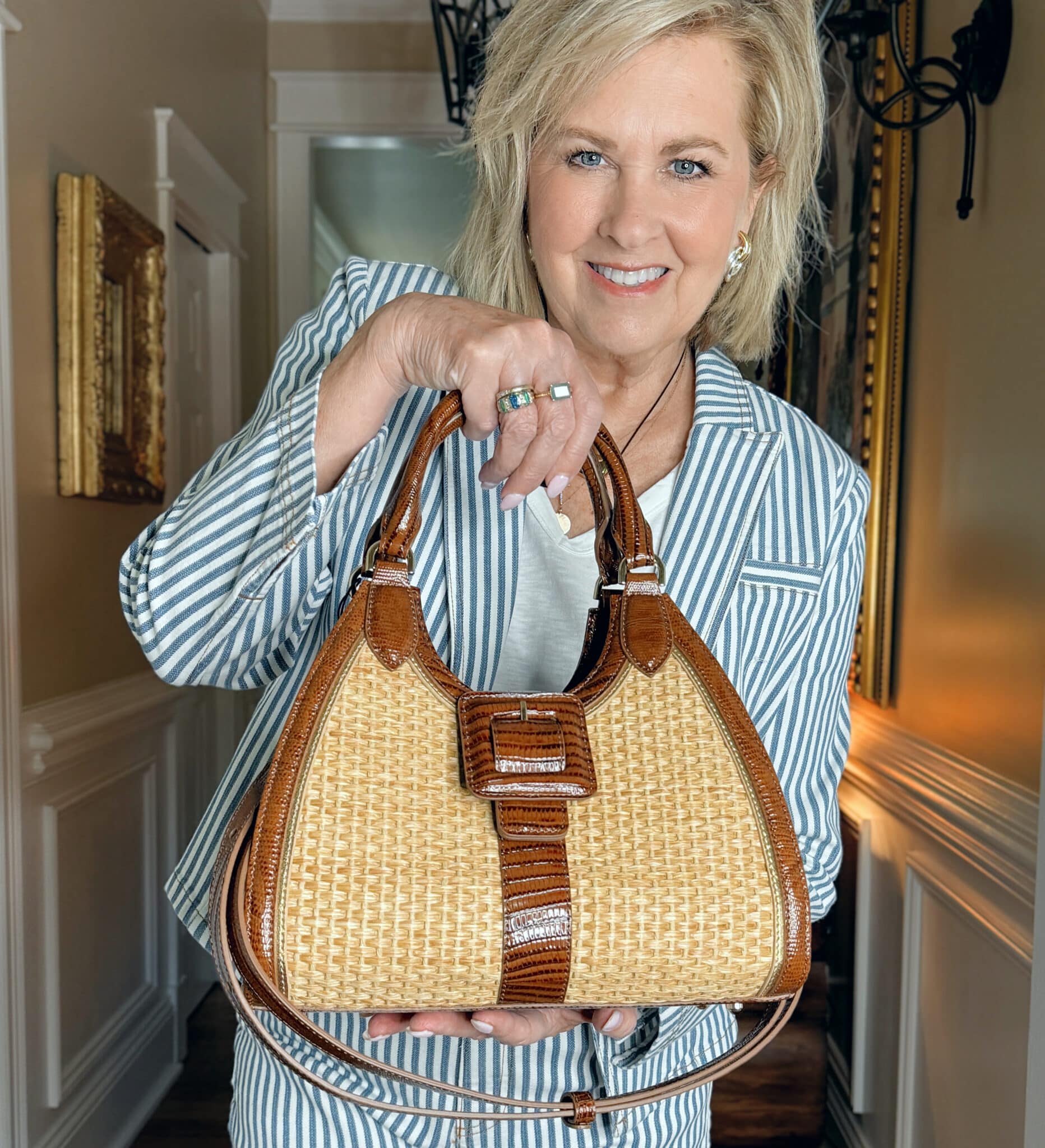 Woman over 50 wearing a striped blazer and holding a Brahmin satchel