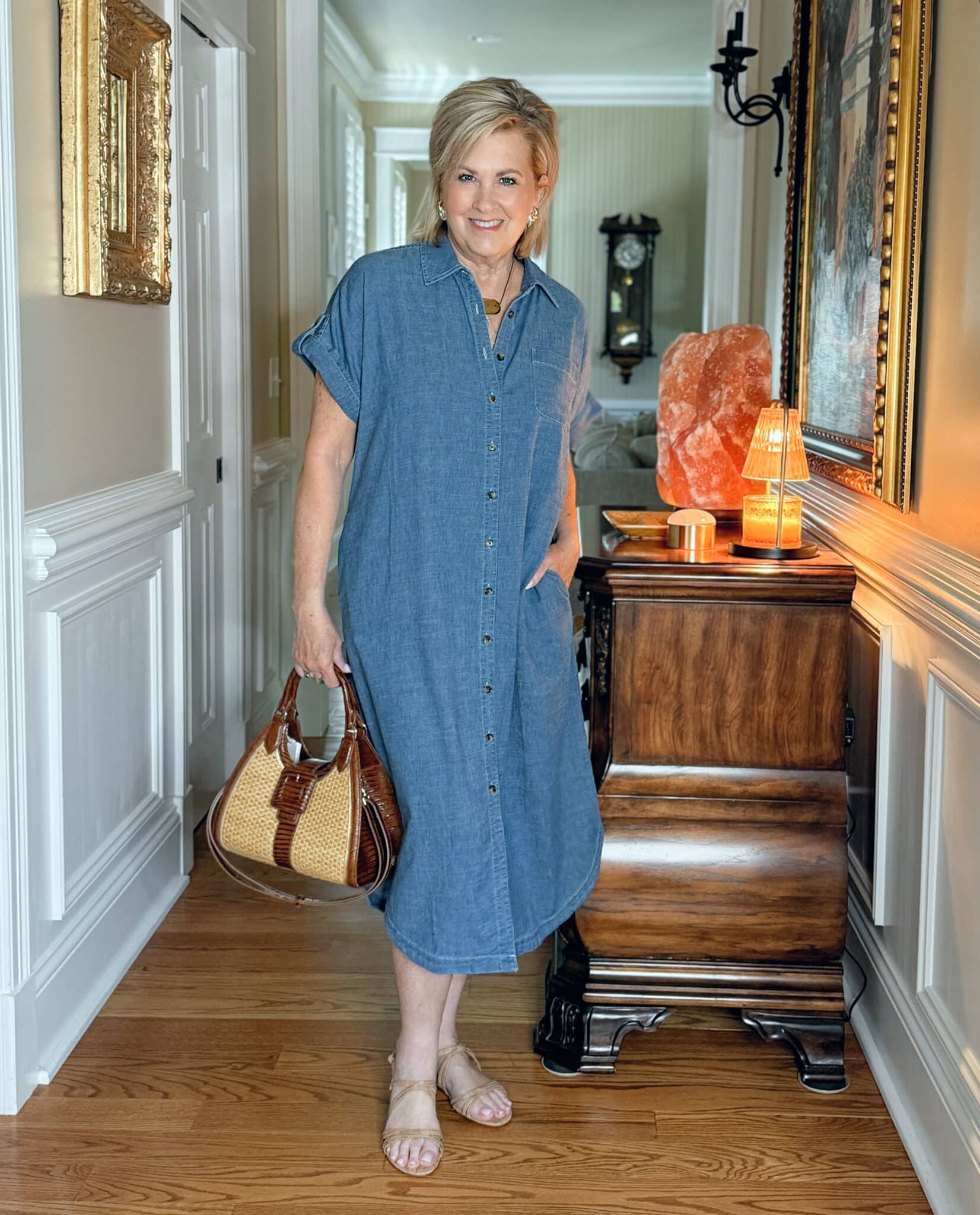 Woman over 50 in a chambray shirt dress with slide sandals, a slouchy cotton crossbody bag, and gold accessories—an easy, one-and-done outfit for warm weather.