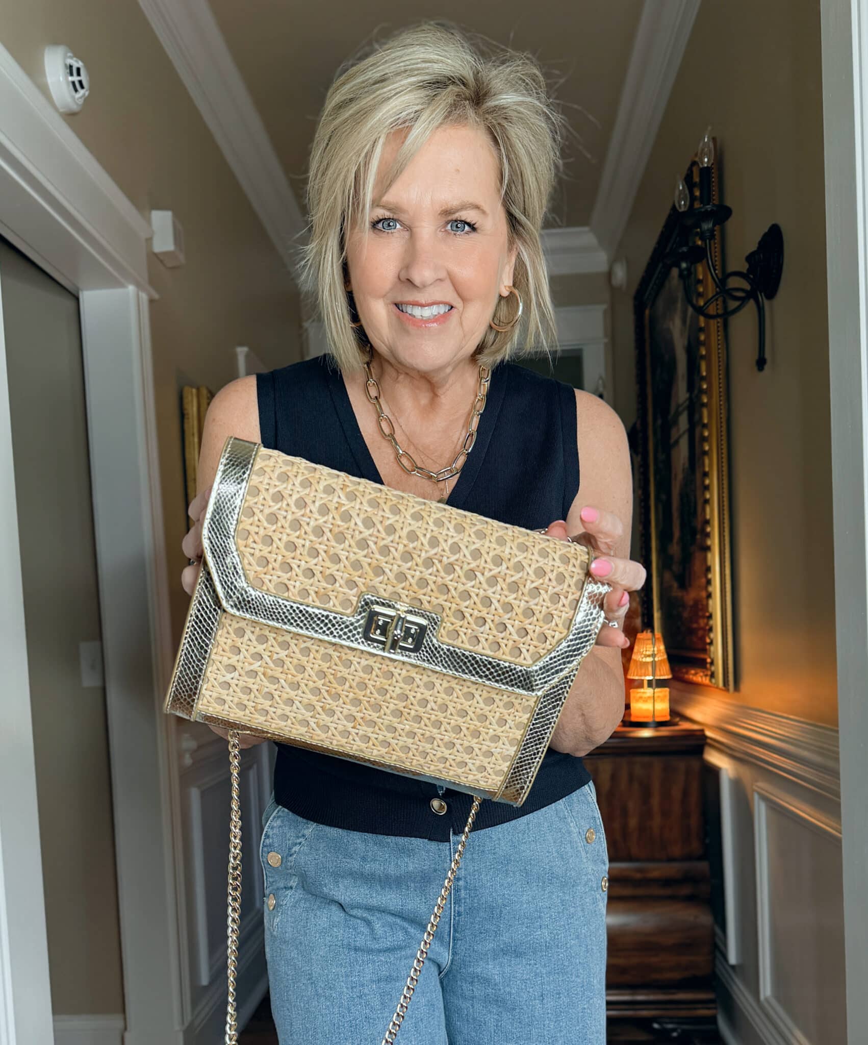 Woman wearing a navy sweater vest and holding a rattan handbag