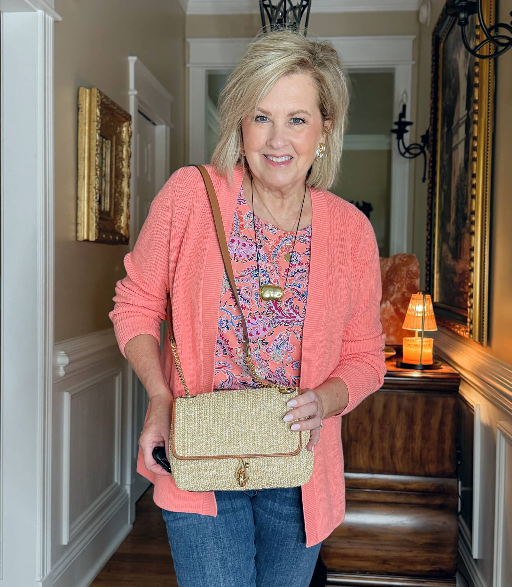 woman wearing a J.Jill a summer outfit with a coral cardigan, a coral printed top, and a straw handbag