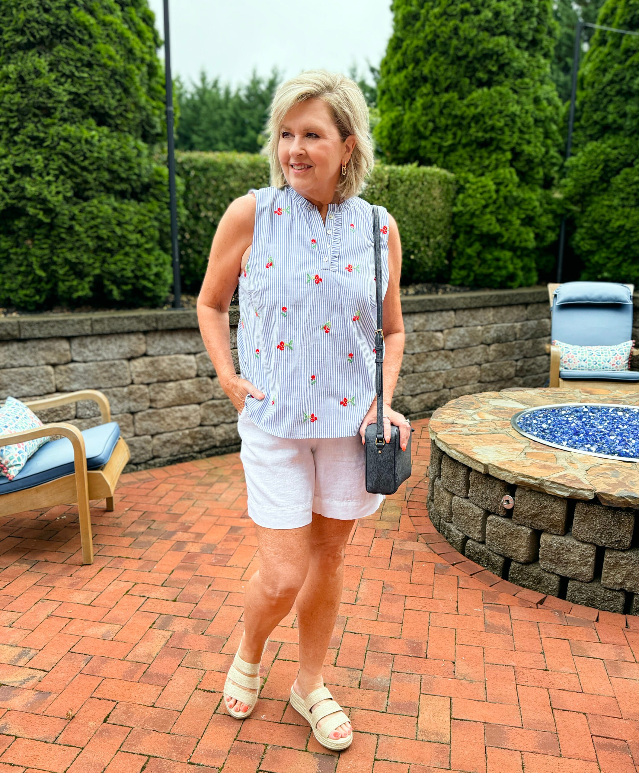 Woman wearing a sleeveless embroidered cherry top with linen shorts and wedge sandals for a casual patriotic outfit