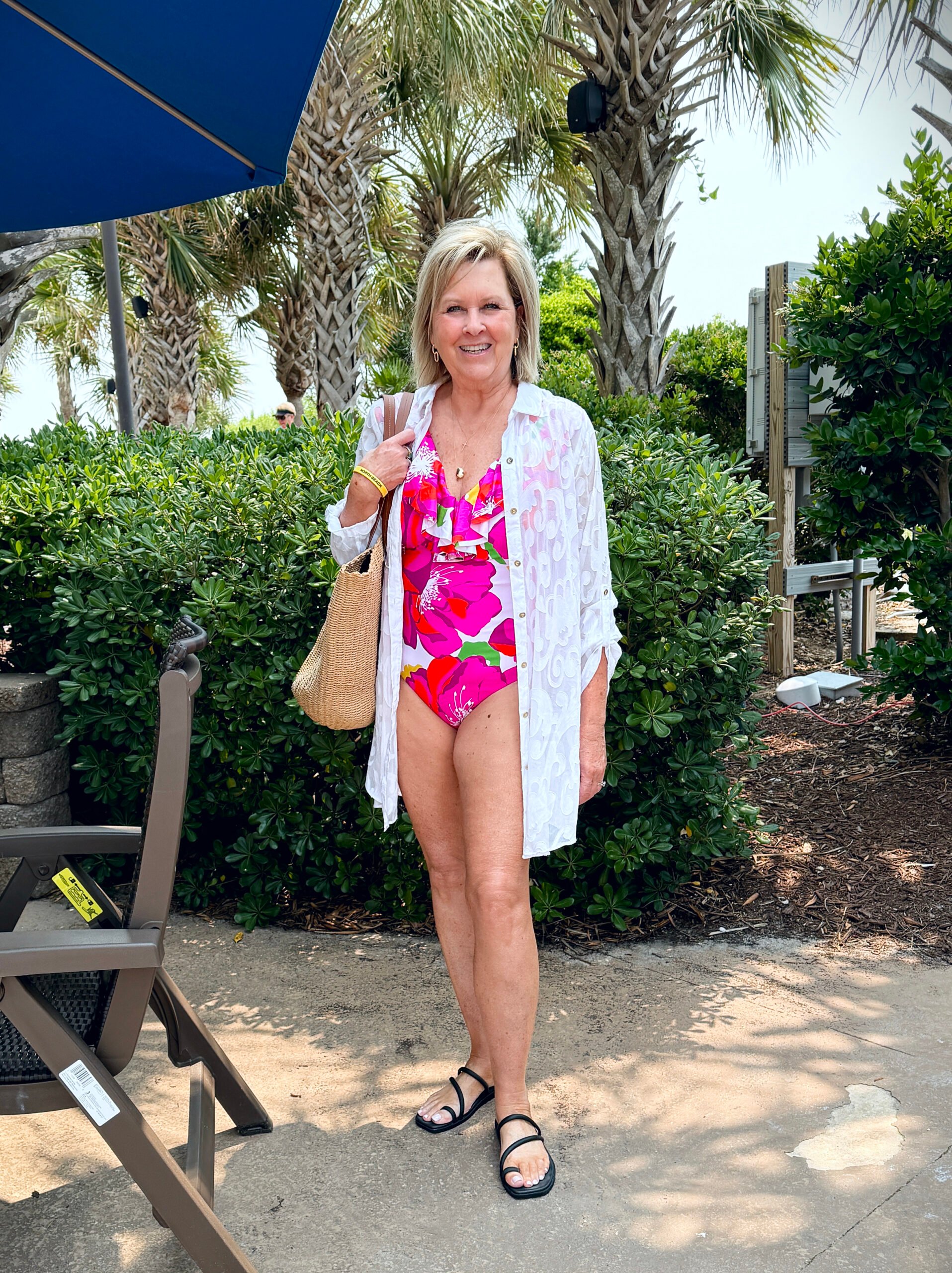 Tania wearing a bright pink Trina Turk swimsuit with a white lace cover-up while on vacation at the beach