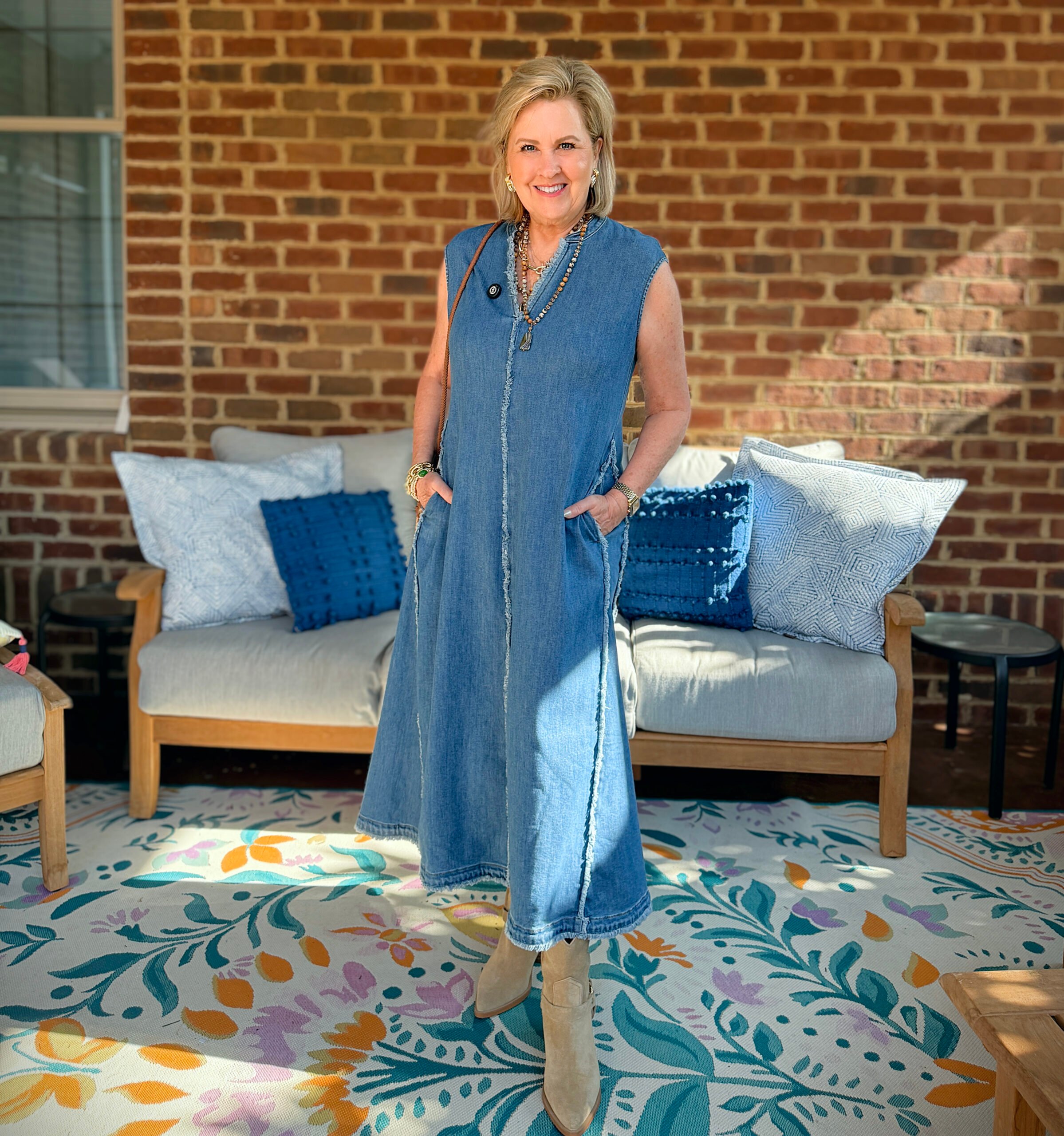 Tania is wearing a frayed denim dress in front of a couch on a porch