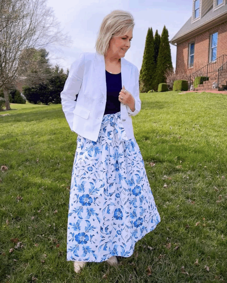 Tania standing in a yard and wearing a white jacket and a white poplin skirt with blue flowers