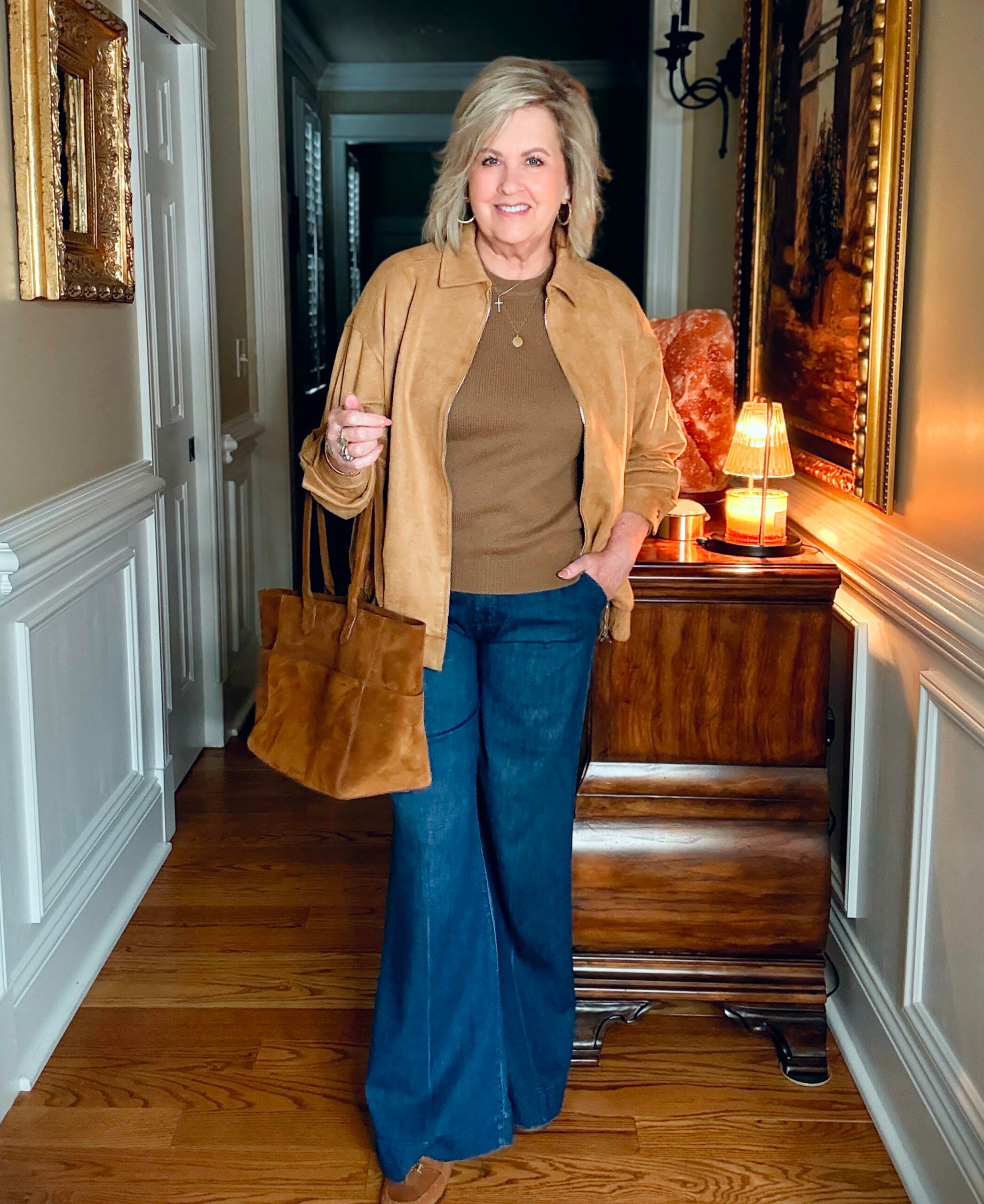 Tania is wearing a camel jacket, a brown sweater, and wide leg jeans