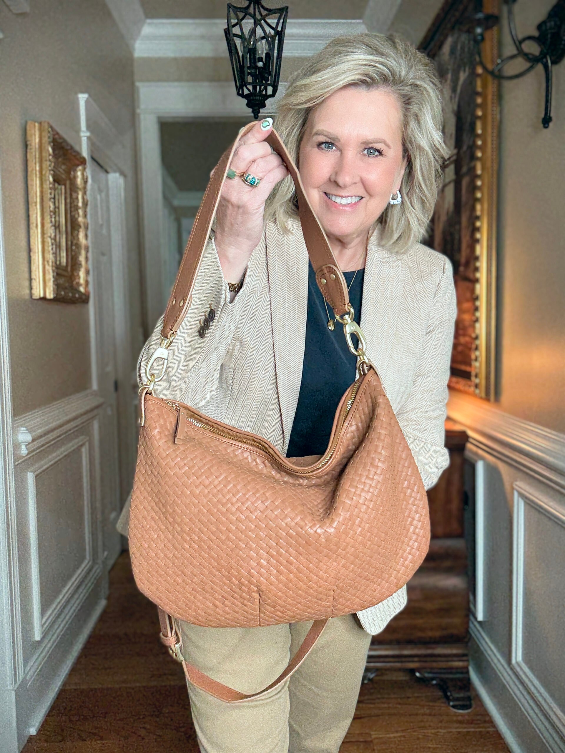 Tania Stephens in a hallway wearing a navy tee, a herringbone blazer, and a woven crossbody bag
