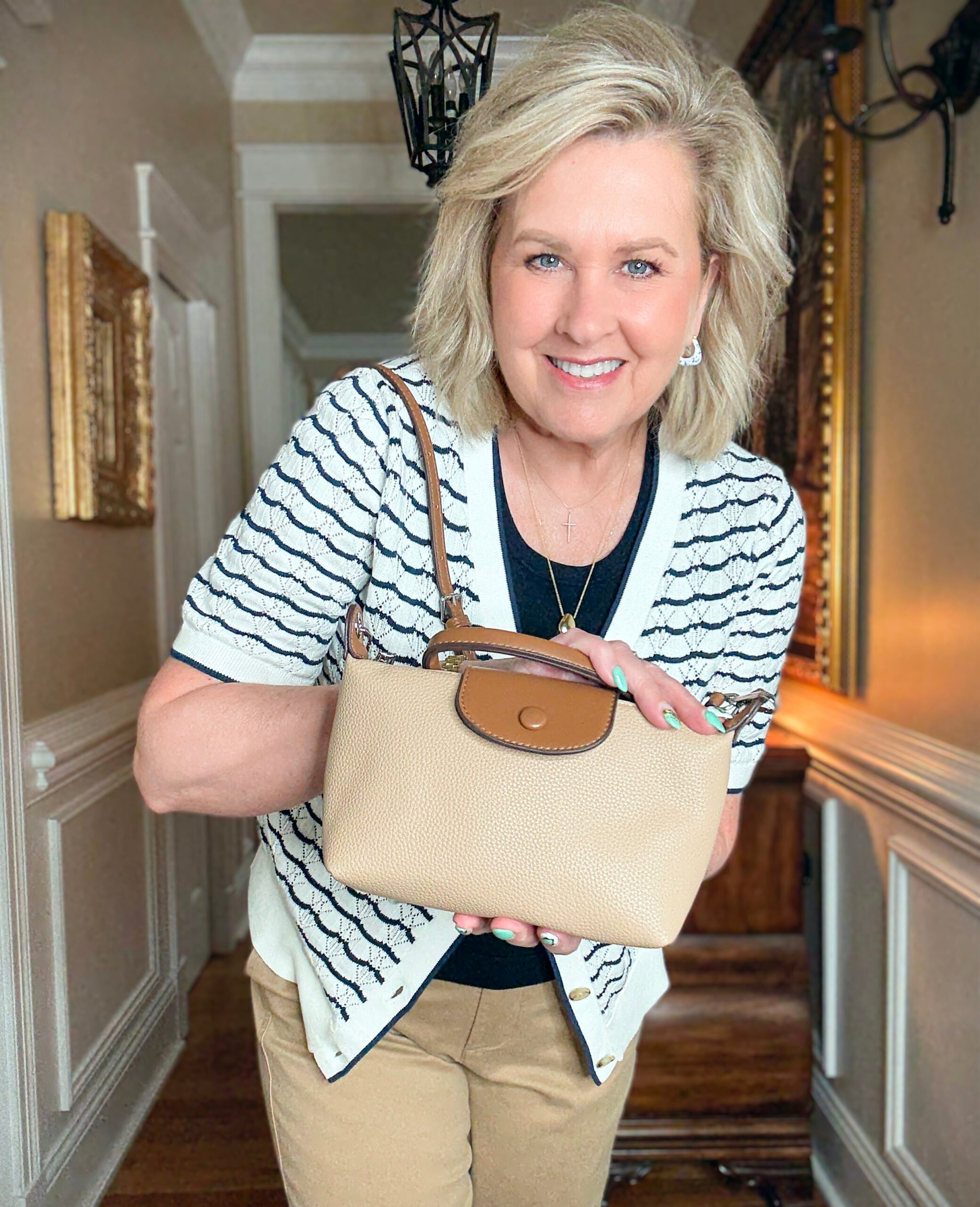 Tania Stephens in a hallway wearing a navy tee and a navy & white cardigan with a small crossbody bag