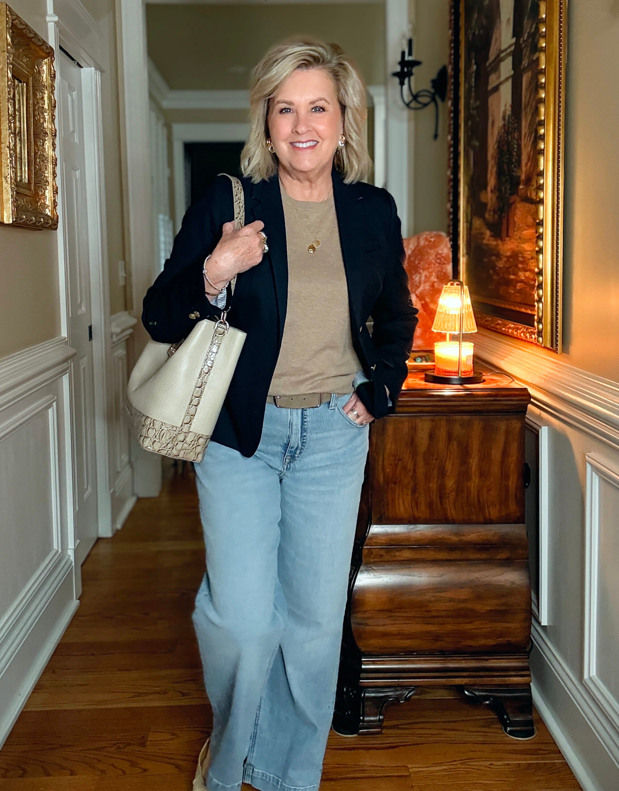 Tania Stephens in a hallway wearing a navy blazer, a beige shell, and a pair of wide leg jeans