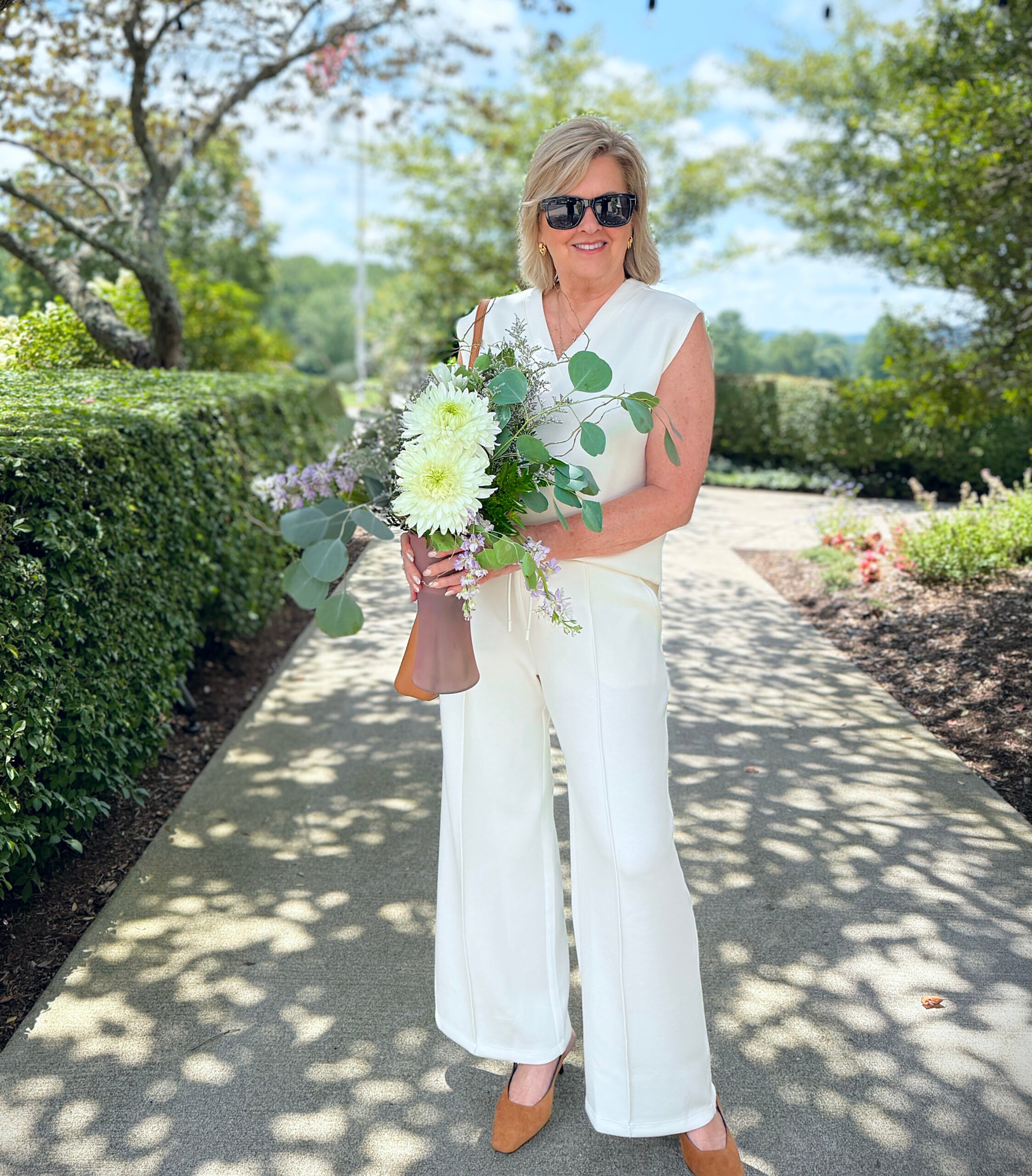 Woman wearing ivory V-neck tank with ivory wide-leg pants, tan crossbody bag, and tan slingback pumps.