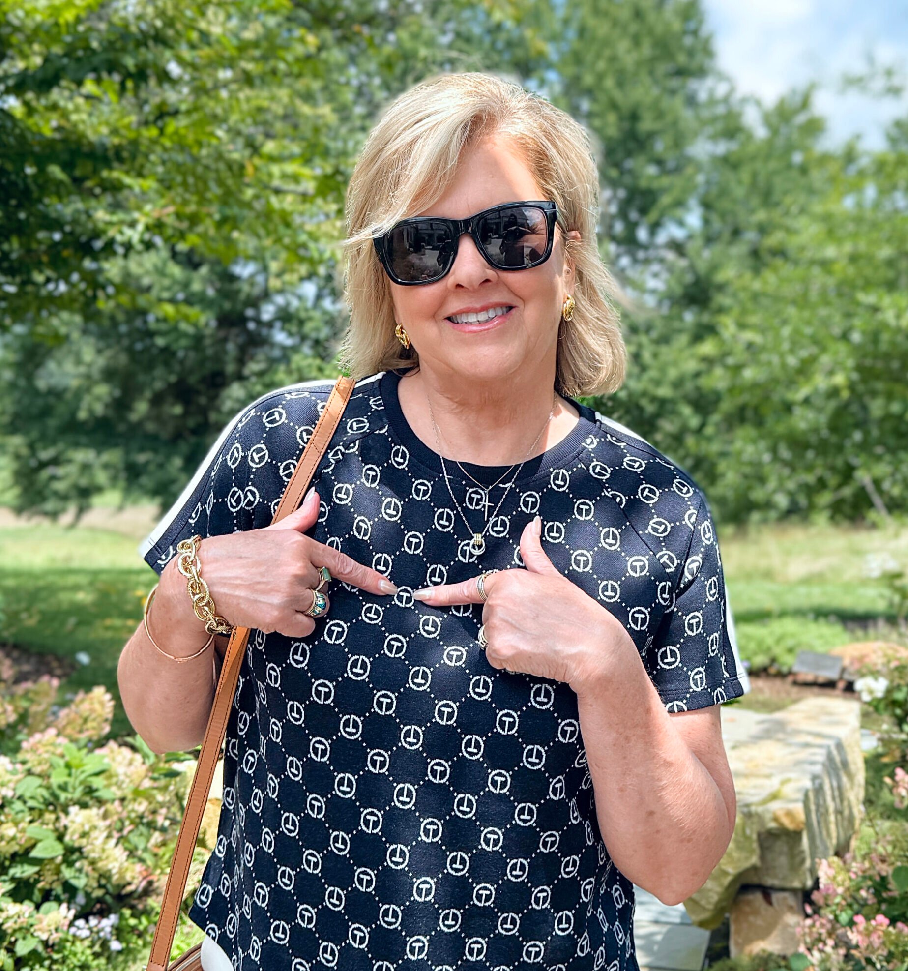 Tania Stephens walking on a garden path in a navy blue top and pointing to the T