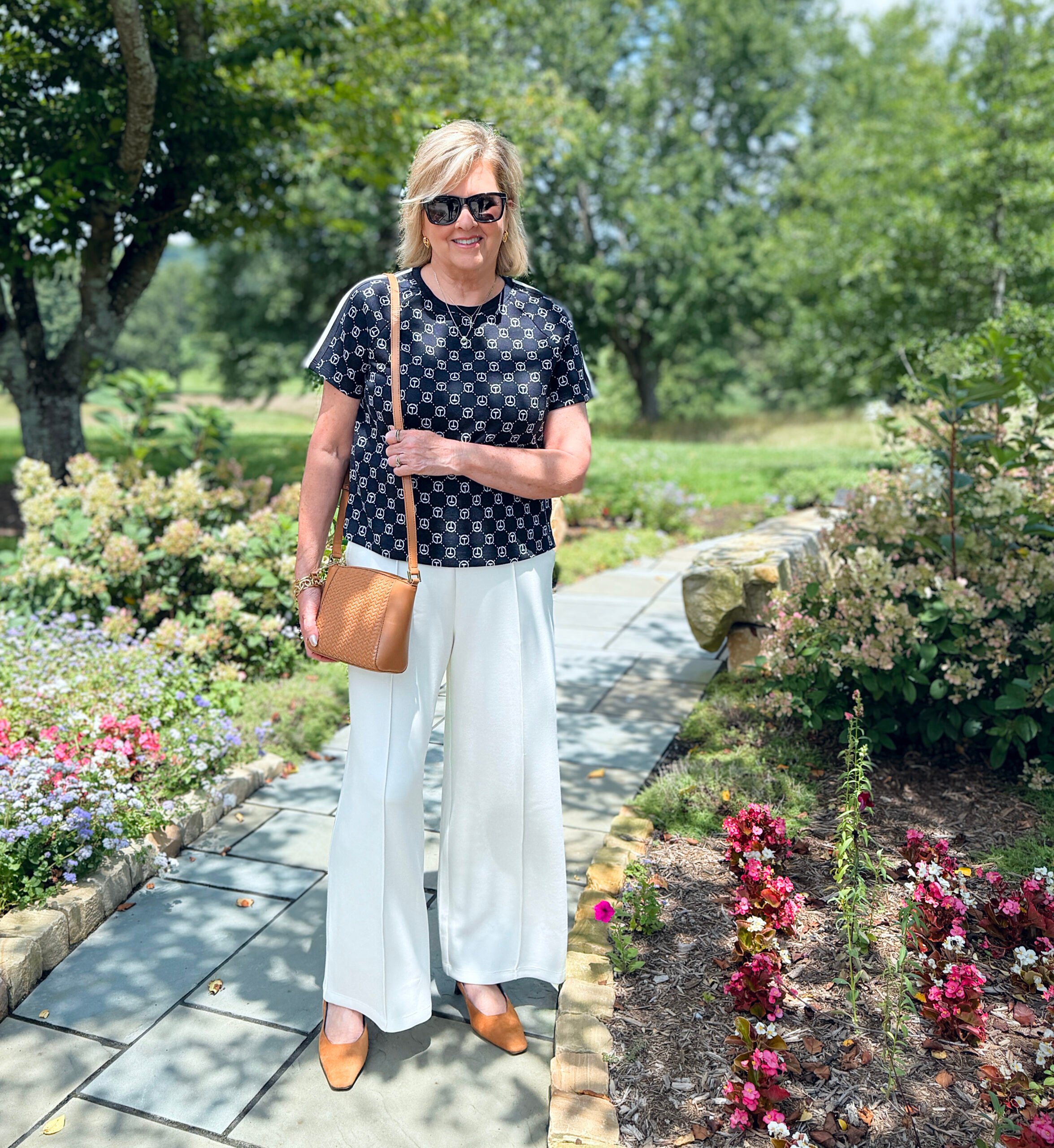 Woman wearing navy logo jacquard tee with ivory wide-leg pants, tan crossbody bag, and tan slingback kitten heel pumps.