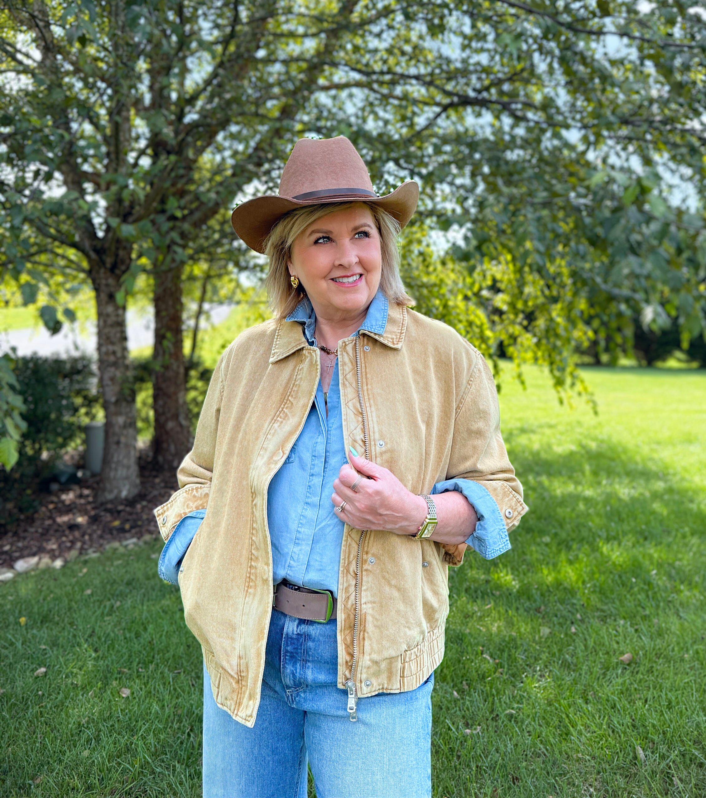Tania wearing a chambray shirt and a brown barn coat with a cowboy hat from Nordstrom Rack