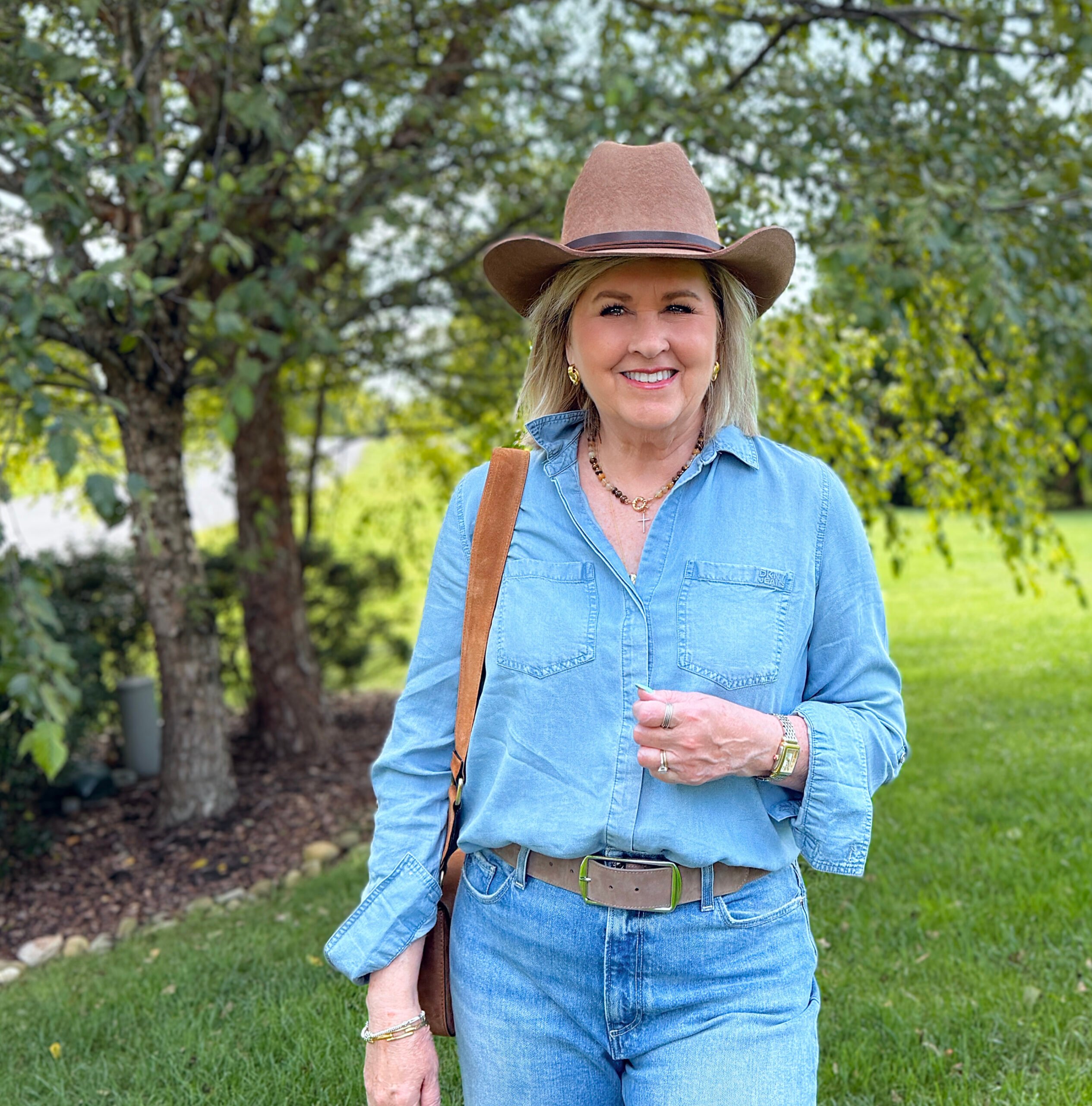 Casual western style outfit for women over 50 with chambray shirt, raw hem ankle jeans, cowboy hat, and suede horsebit crossbody bag from Nordstrom Rack.