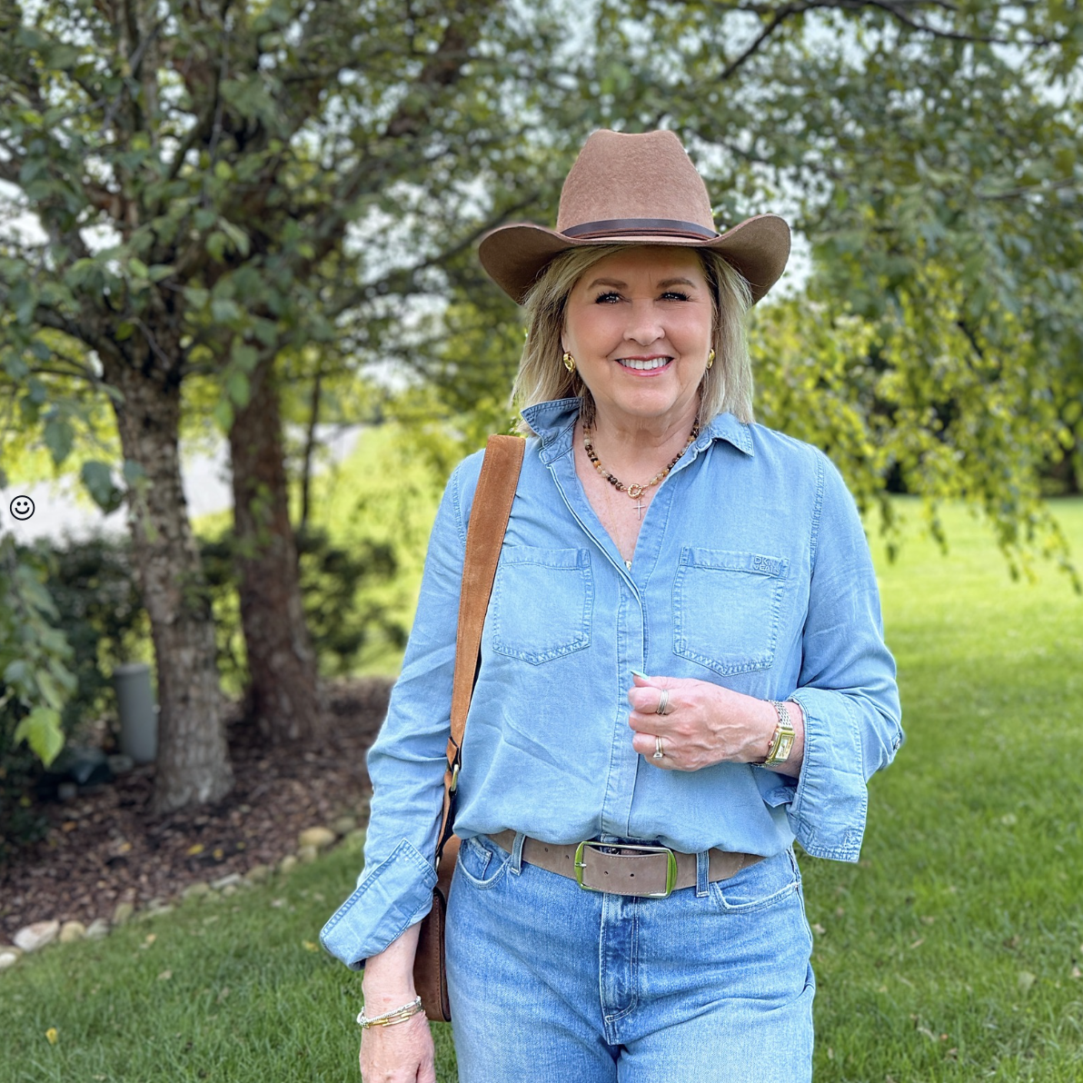 Casual western style outfit for women over 50 with chambray shirt, raw hem ankle jeans, cowboy hat, and suede horsebit crossbody bag from Nordstrom Rack.