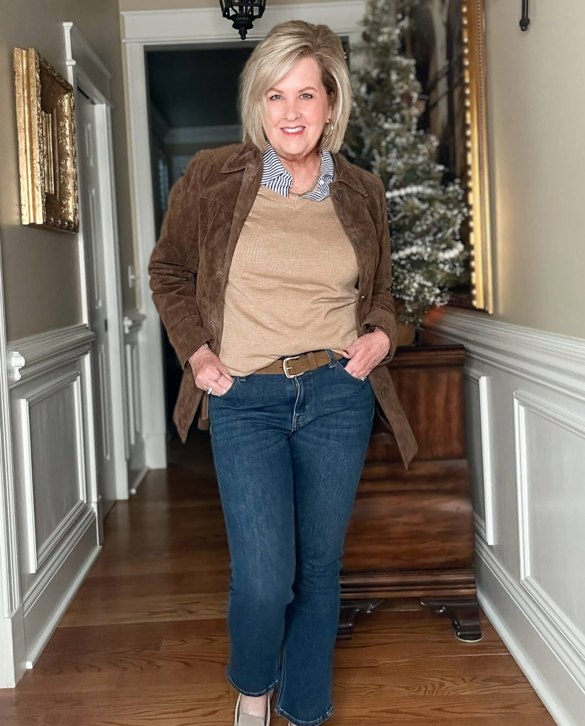 Tania Stephens wearing a dark brown suede jacket, a camel sweater, striped button up shirt, and a pair of jeans