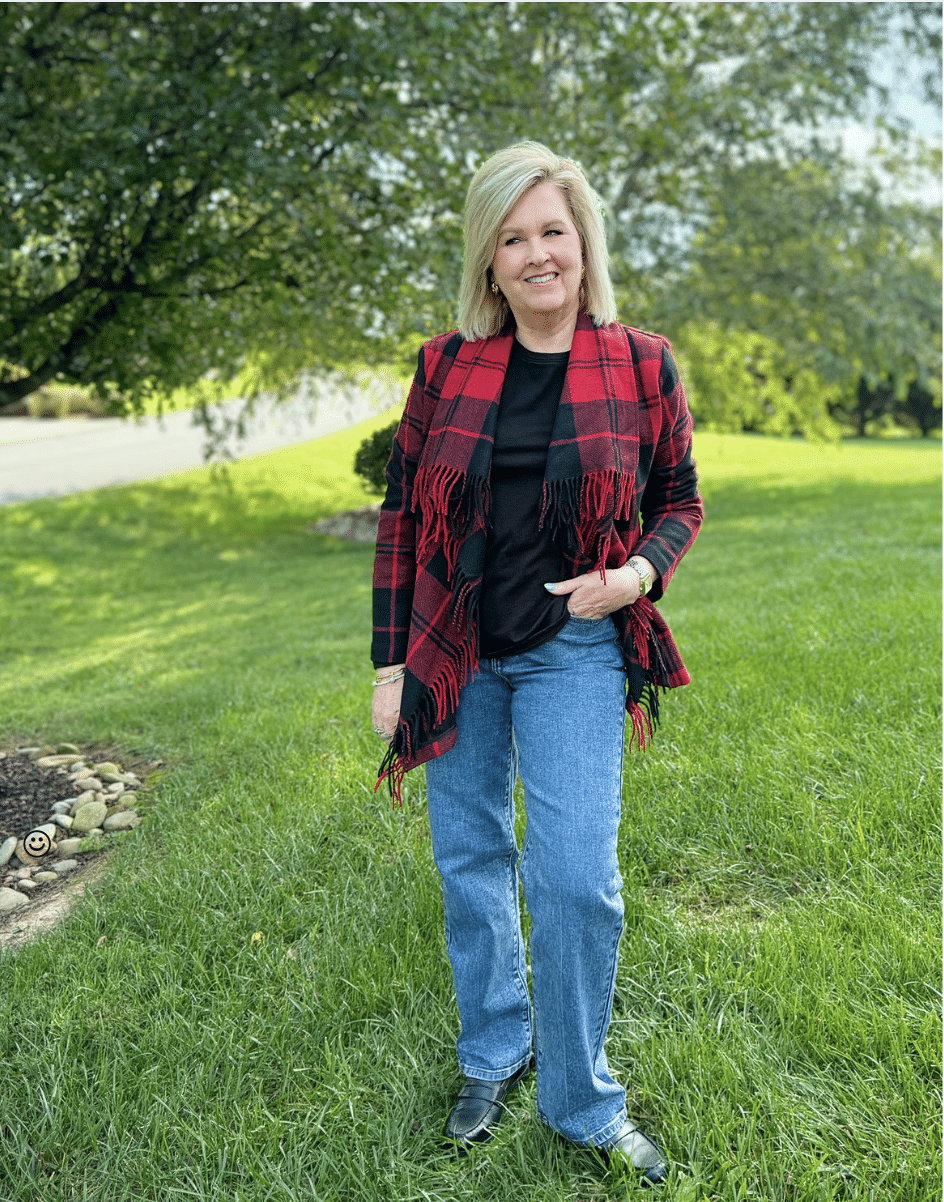 Woman over 50 standing in a grassy field wearing a black tee with a red and black shawl jacket with fringe and straight leg jeans from Kohl's