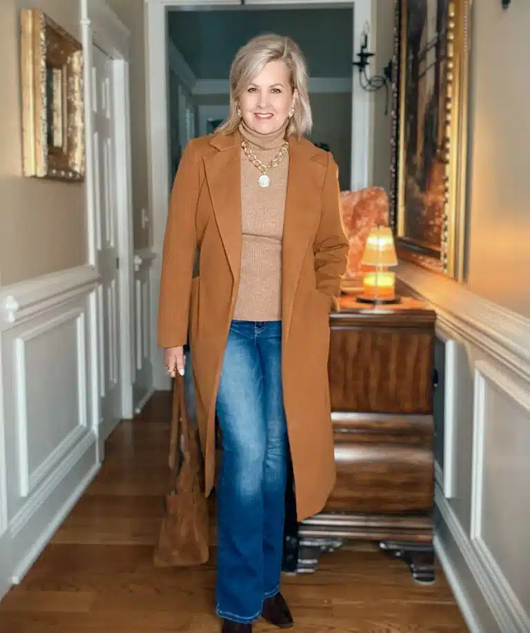 Tania wearing a camel sweater and jeans with a long caramel coat for a Thanksgiving Outfit