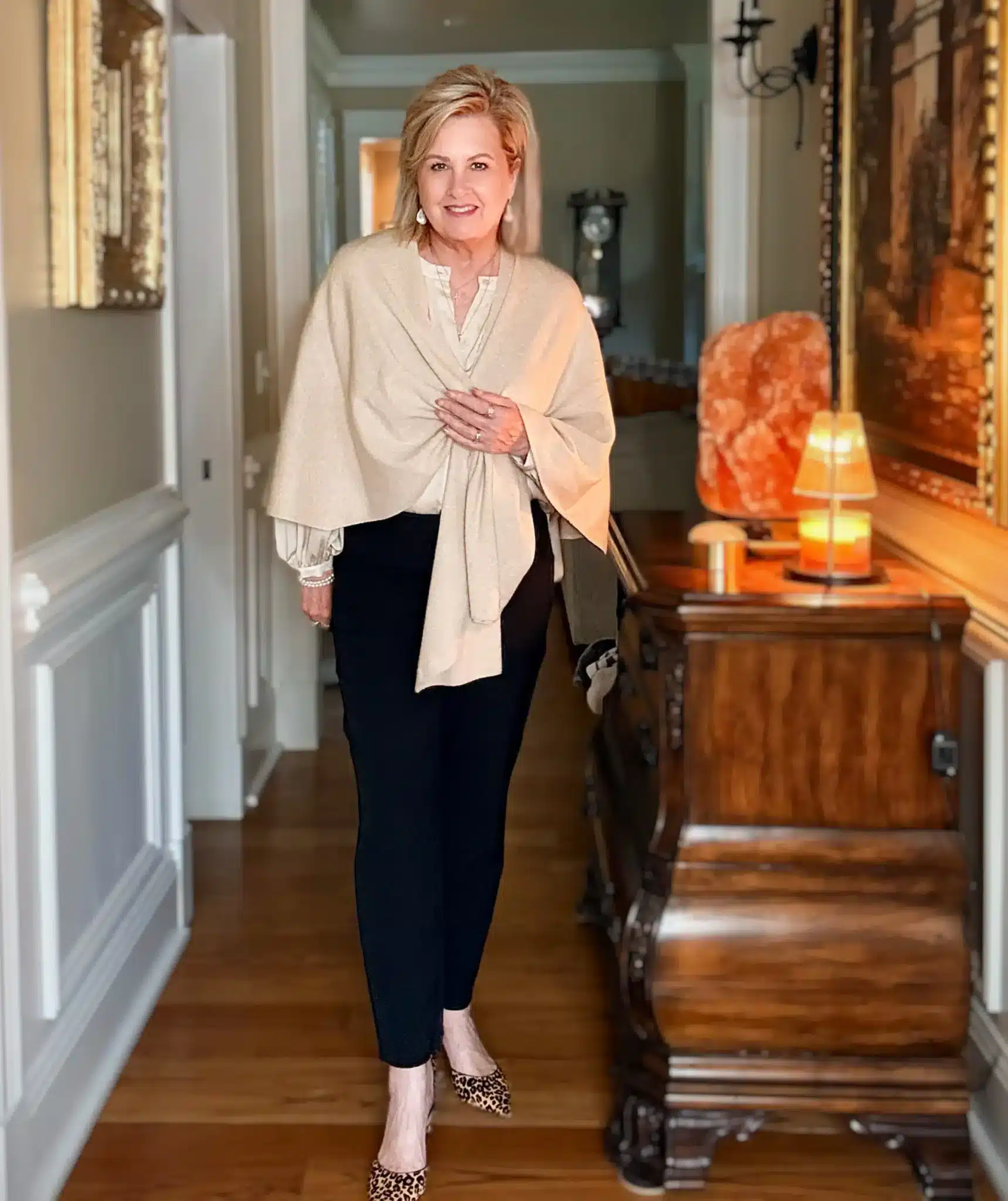 Tania wearing a beige wrap over a cream blouse and black pants with leopard heels, a classic and cozy Thanksgiving outfit.