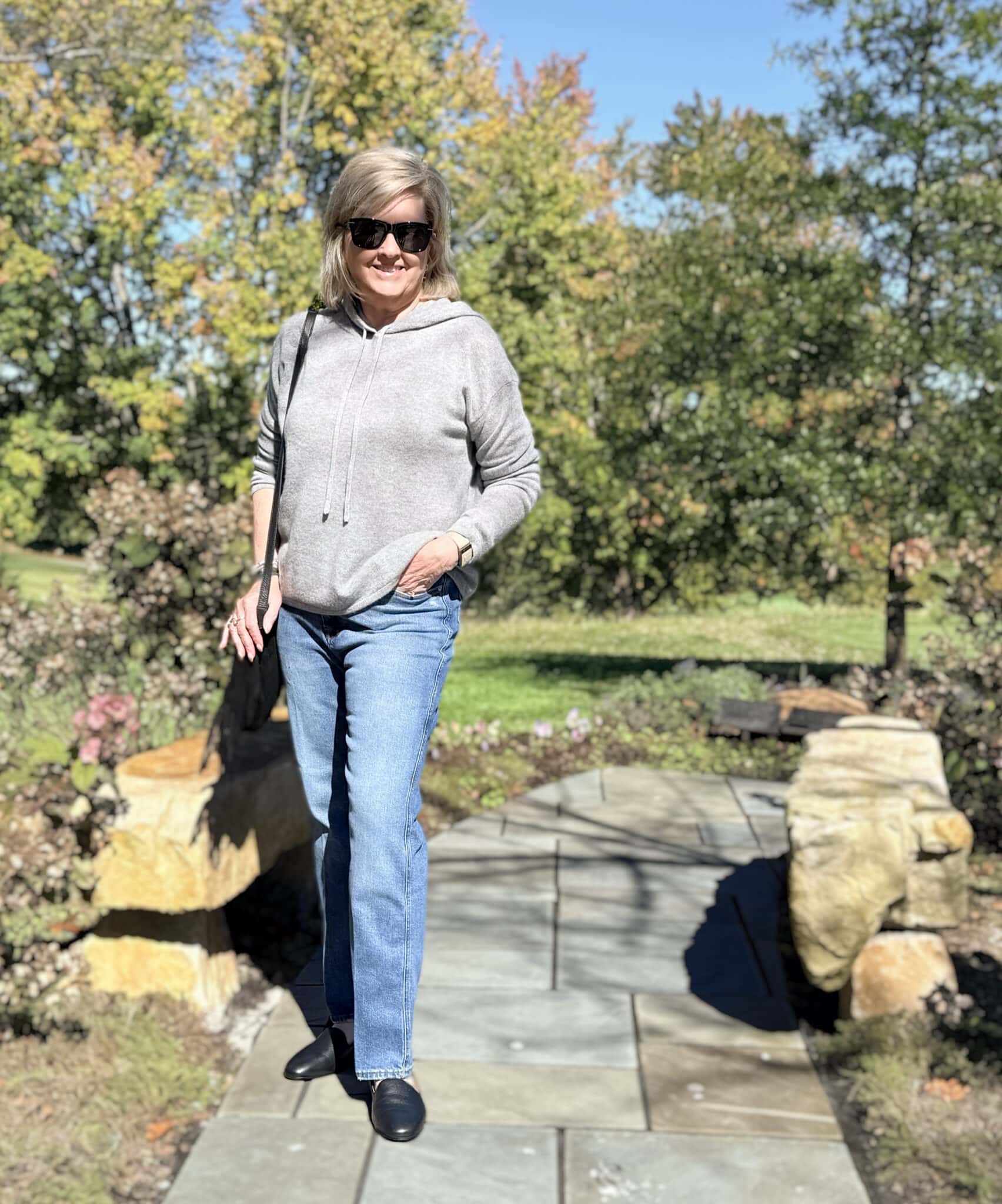 Tania Stephens in casual weekend outfit for women over 50 wearing a cozy sweater and jeans, while walking on a slate path