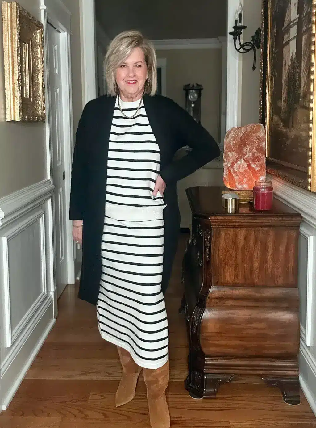 Tania wearing a black and white striped sweater dress with a long black cardigan and tan boots, a stylish and comfortable Thanksgiving outfit.